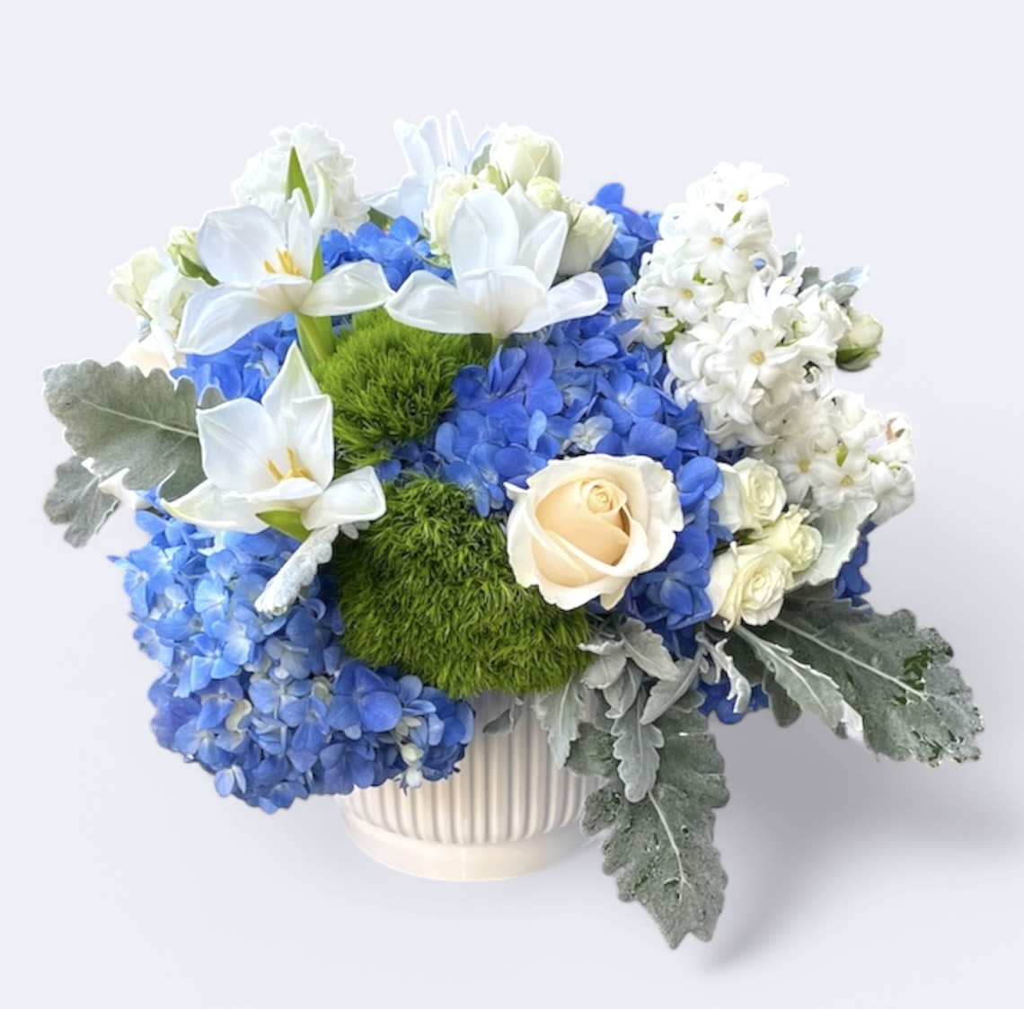 Spring Rain  - This wonderful arrangement is made up of blue hydrangeas, white roses, hyacinths, tulips, spray roses, dusty miller leaves, and dianthus. 