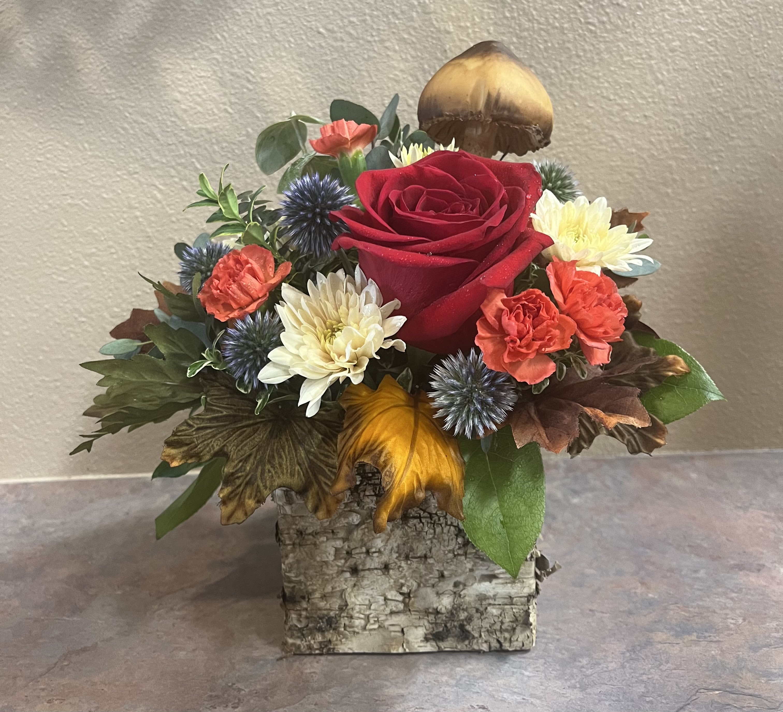 In The Woods - This arrangement is a mix of colorful flowers with a woodsy, natural twist. Perfect for every occasion and every person. It is presented in a rustic 4.5&quot; X 4.5&quot; bark covered, wooden cube. Topped with a mushroom pick for a flair of whimsy. 