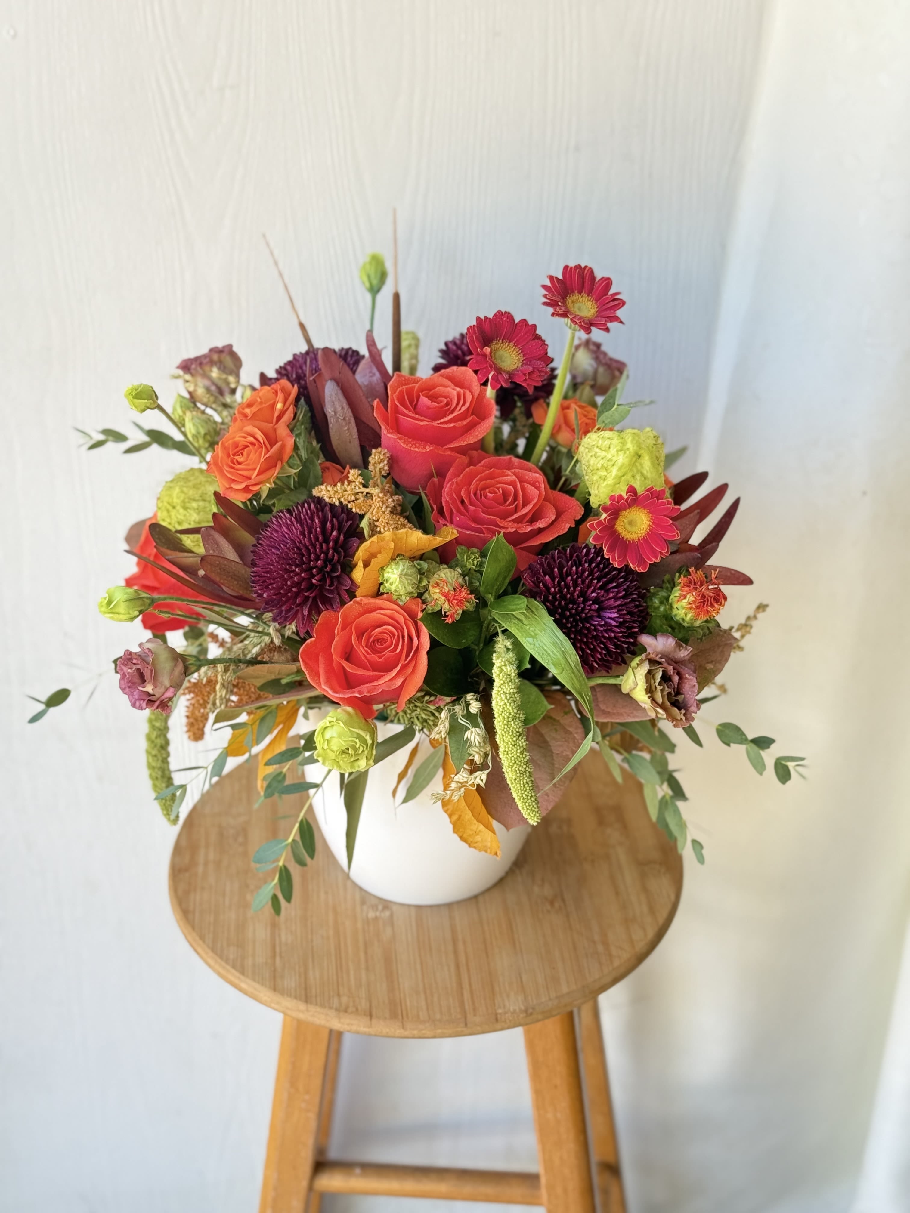 EC47 - Colors of Fall - Bring the warmth and beauty of autumn into your home with our stunning Colors of Fall arrangement . This  compact design features a variety of fall foliage and leaves, accented by vibrant orange roses, orange lilies , hypericum berries and autumn leaves and foliage.The arrangement is expertly crafted in a ceramic bowl container, adding a touch of glamour to the natural beauty of the fall blooms The rich color of  fall also perfectly complements the warm tones of the flowers and foliage.Perfect for any fall occasion, from Thanksgiving dinner to a cozy autumn night in, our Colors of Fall will bring the essence of the season into your home.
