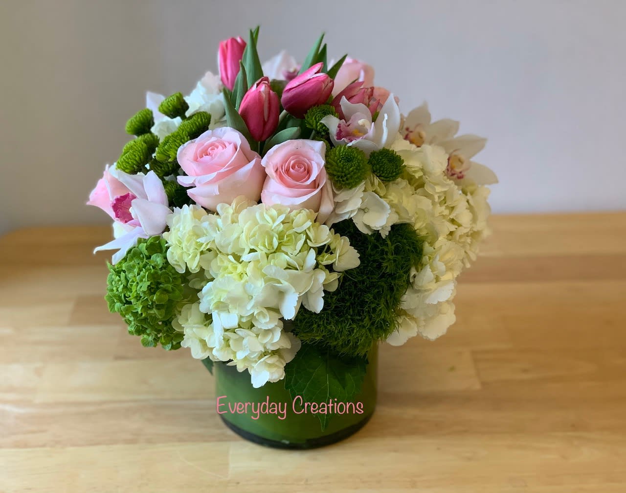 EC27 - Simple Beauty  - The Simple Beauty flower arrangement is the perfect combination of romance and sophistication and includes soft pink roses, white hydrangeas and delicate pink tulips. These fresh blooms are gorgeously arranged with vibrant green button mums which add texture and depth to the bouquet in a modern glass vase wrapped with a bright green leaf. This one-of-a-kind floral arrangement is a perfect choice for any special occasion, including weddings, birthdays, baby showers or even just an elegant and beautiful housewarming gift. 