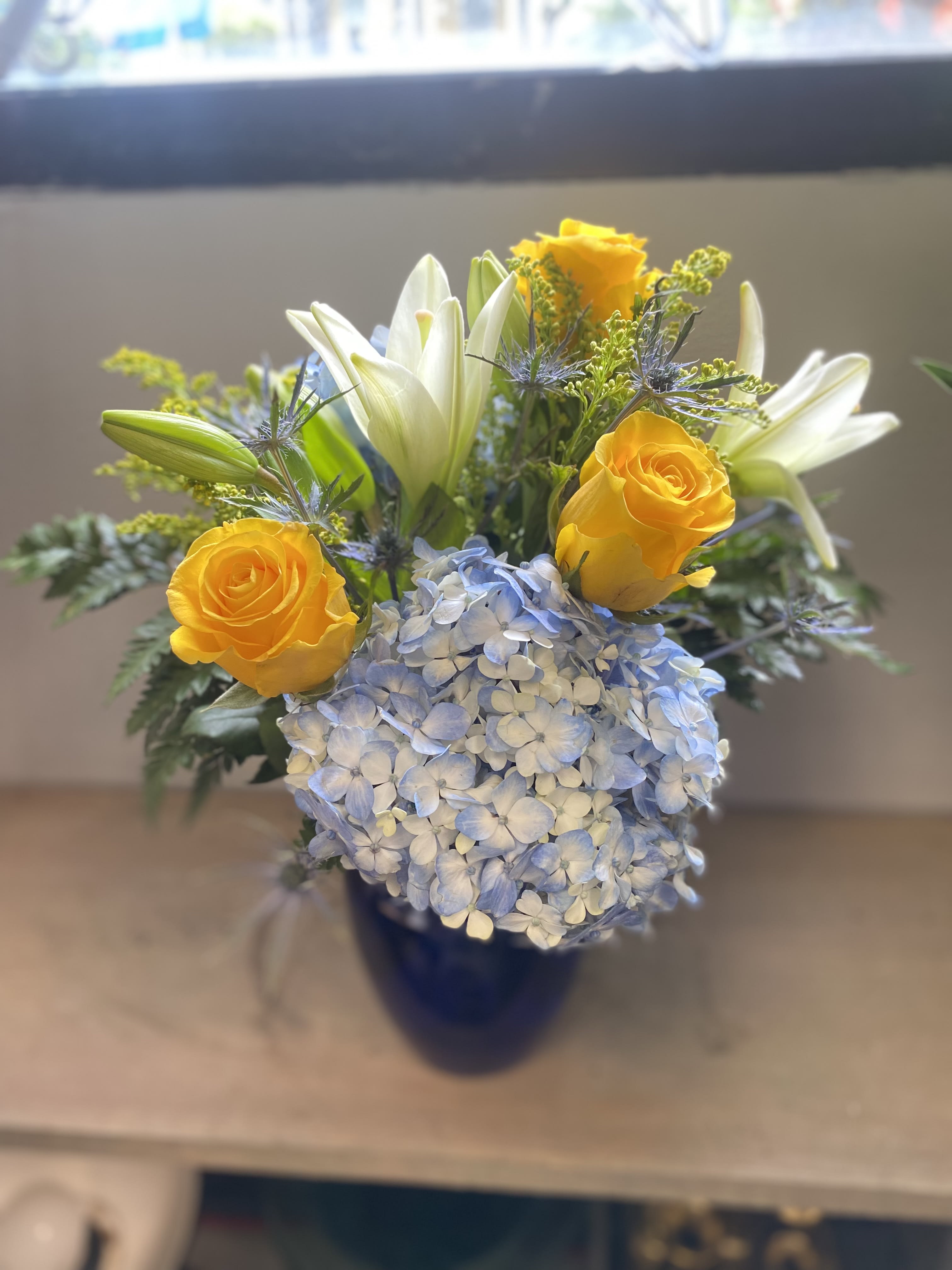 Blue Skies Bouquet with roses Blue Skies Bouquet with roses - Yellow roses, blue hydrangea, lilies and assorted fillers and foliage designed in a vase.