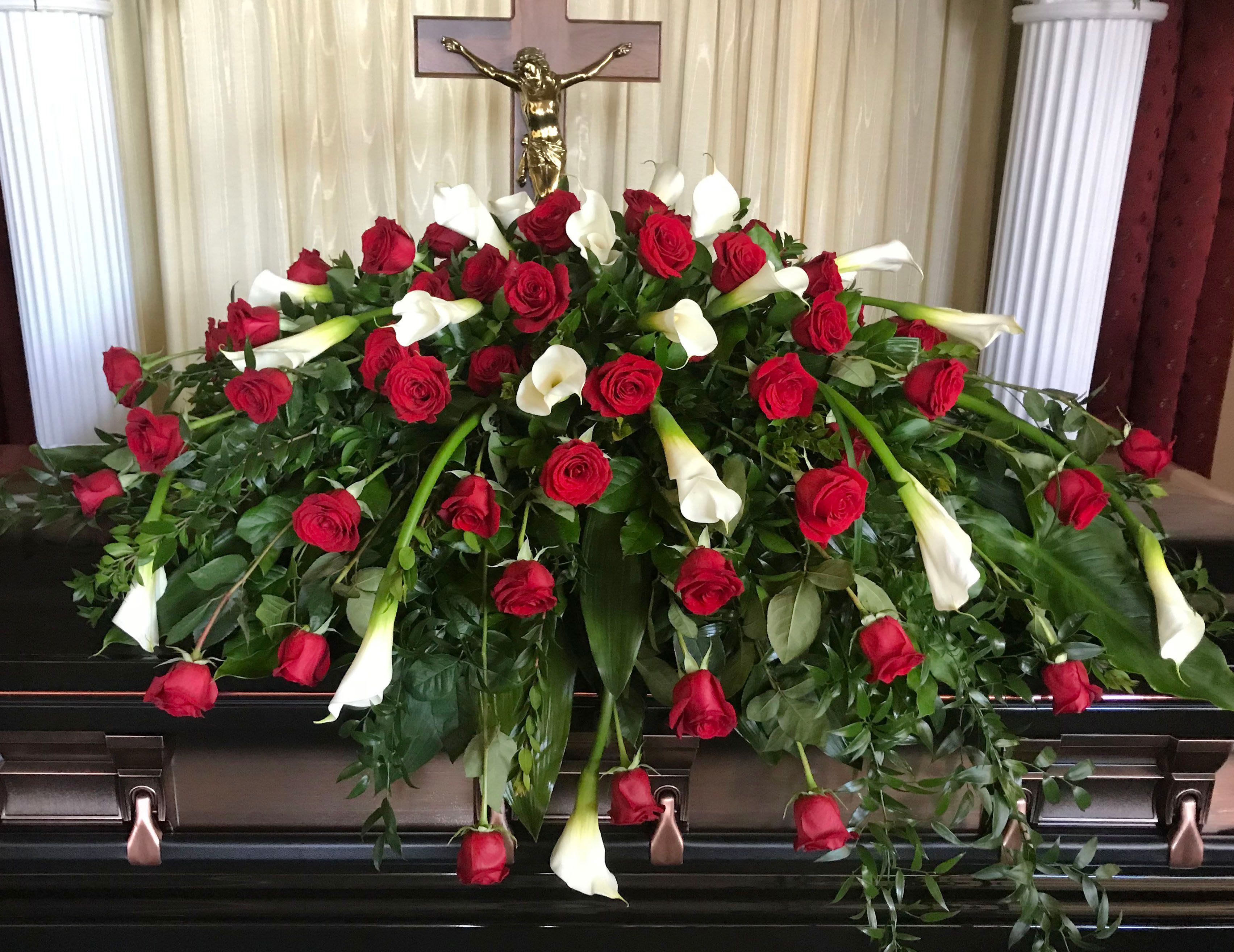 Casket Spray CS-20 Casket Spray CS-20 - Graceful and reverent, this casket spray combines classic red roses with elegant white calla lilies, symbolizing deep love, purity, and eternal peace. Designed with lush greenery and a flowing silhouette, this tribute exudes timeless beauty and spiritual significance.  Perfect for honoring a beloved spouse, parent, or someone deeply cherished, this arrangement is ideal for faith-based services or those seeking a bold yet graceful farewell.  We can change the rose color.   *Photo is of closed casket (deluxe) option.