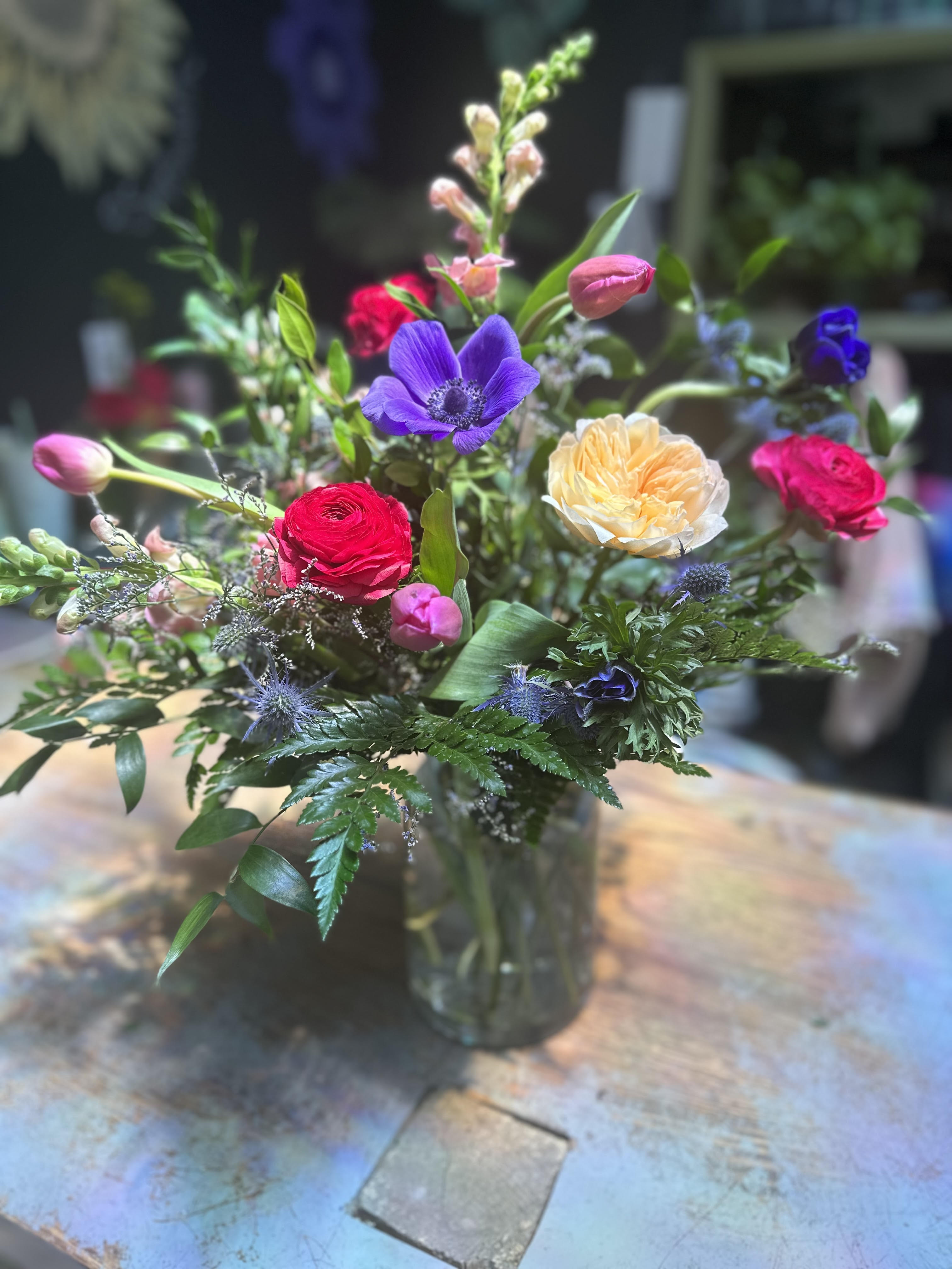 Rocky Mountain Romance - Designed using blue anemones, peachy Juliet garden roses, pink snapdragons, hot pink ranunculus, purple tulips, and silver blue thistle, with lush, textural foliage.