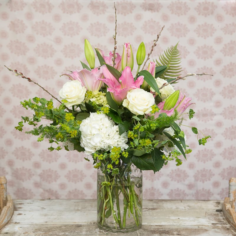 Timeless Beauty Timeless Beauty - Garden style arrangement , bursting with pink lilies accented with white roses and hydrangeas. This bouquet brings sophistication as its presented in a beautiful clear cylinder vase. Perfect for Mother's Day, a spring anniversary or Birthday !