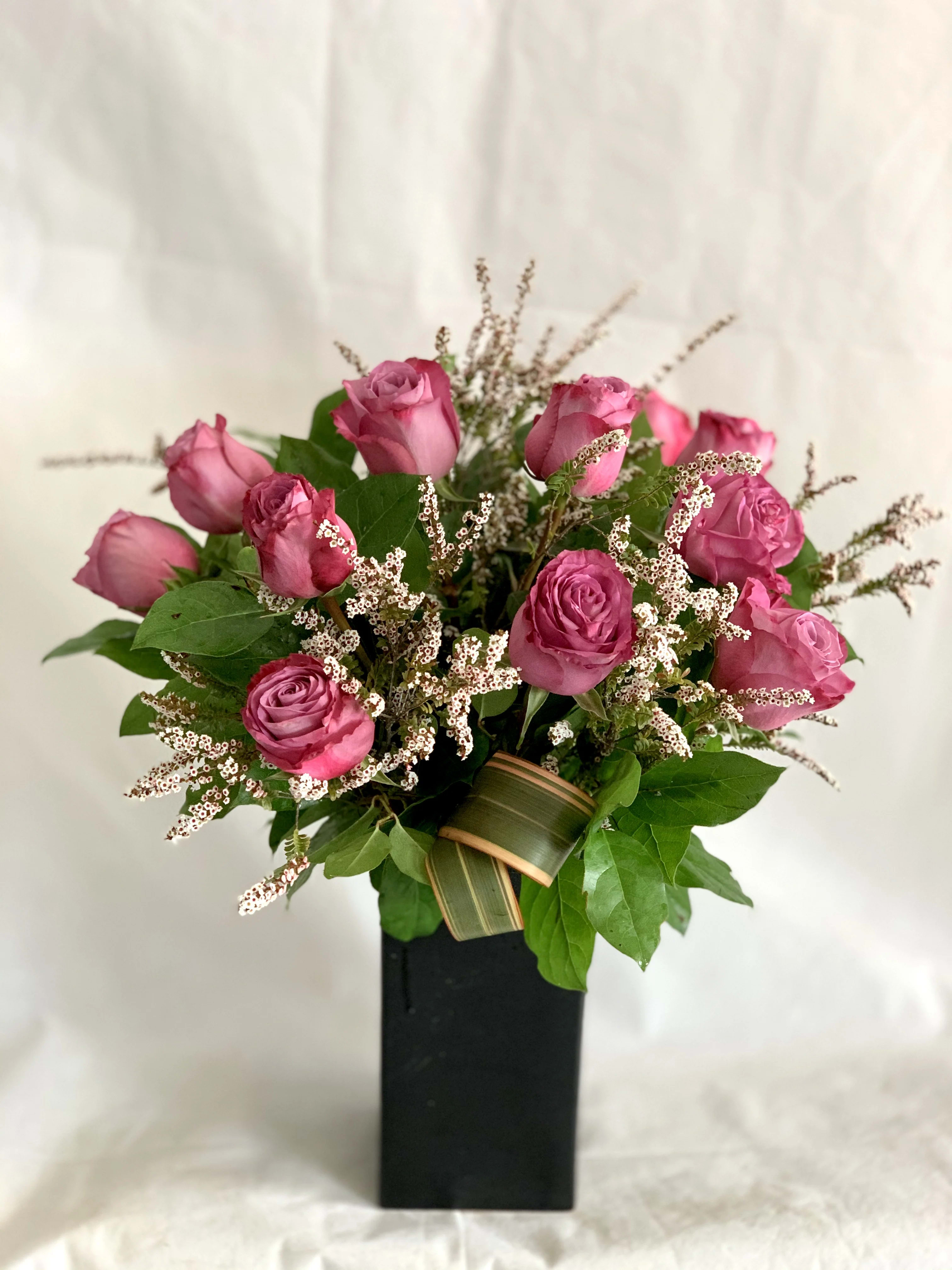 Purple Rose Arrangement Purple Rose Arrangement - A classic rose arrangement with modern styled greens. First 3 pictures are 1 dozen roses. Deluxe has 18 roses. Third picture is Premium with 2 dozen roses Container and fillers may vary depending on season and availability.