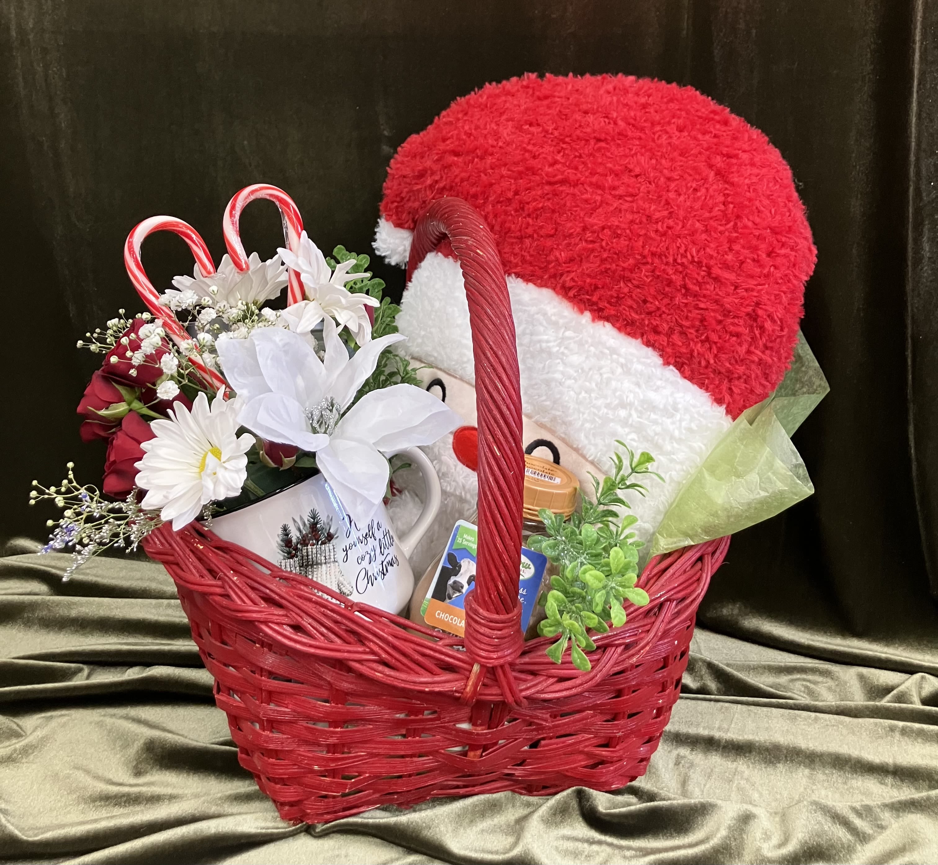 Cozy Comforts Gift Basket Cozy Comforts Gift Basket - Cheerful red basket, feel good items include hot chocolate, a candle, soft Santa pillow and a mug of fresh flowers