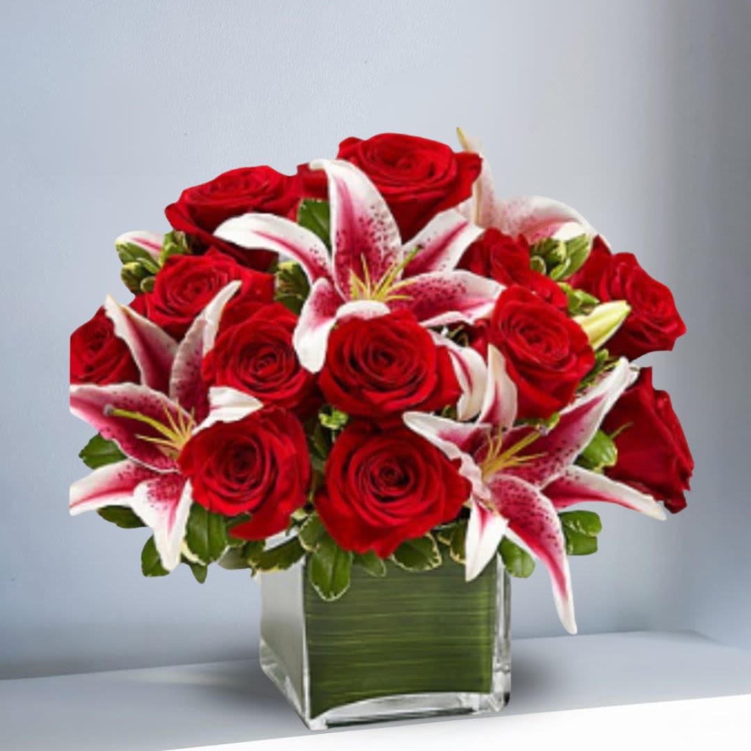 Embrace Moments - Send this truly original, contemporary bouquet of gorgeous red roses and elegant lilies, hand-arranged in a stylish glass cube vase, and she'll think it's the perfect accessory for her modern sensibility. Hand-crafted arrangement of romantic roses and lilies, accented by variegated pittosporum Designed by our expert florists in a modern clear glass cube vase wrapped with an exotic  leaf; vase measures 5&quot;H x5 wide.