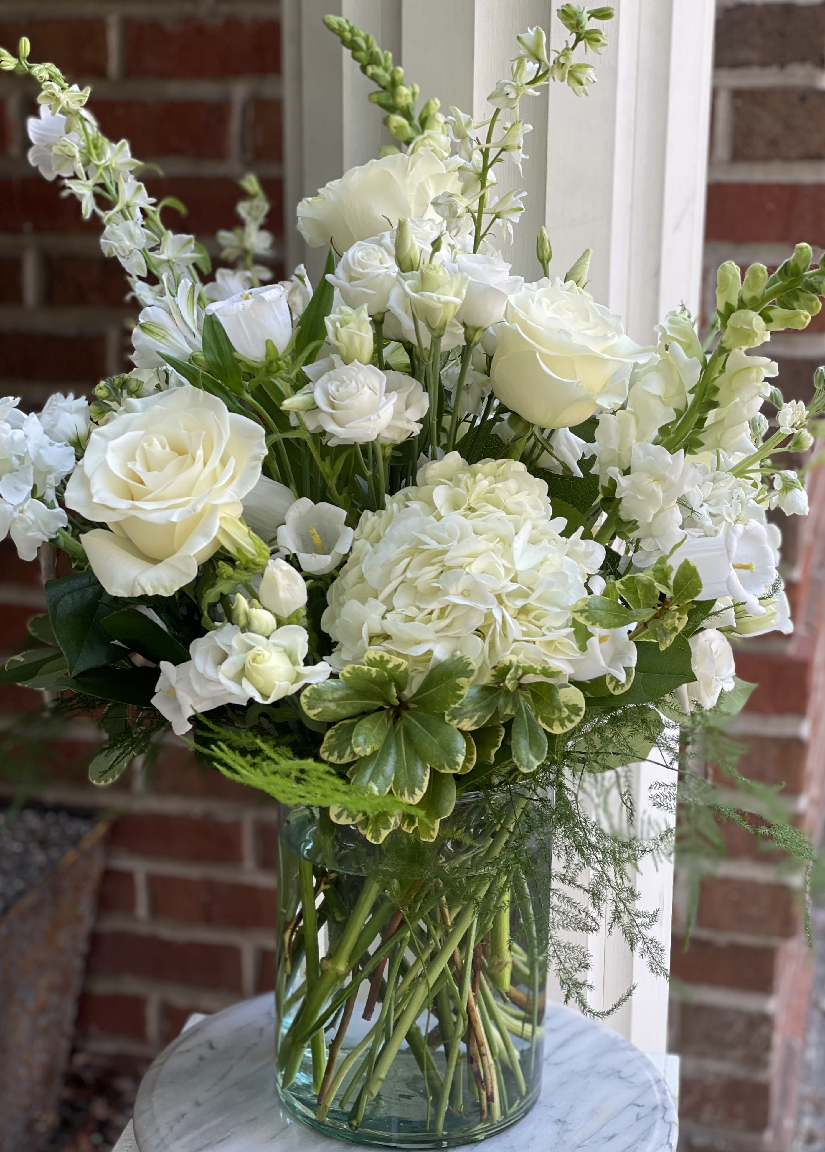 It’s Sympathy  - All white, beautiful arrangement with seasonal blooms and interesting greens. Perfect for the home, church or funeral home.the arrangement will reflect the picture but blooms may change with the seasons.