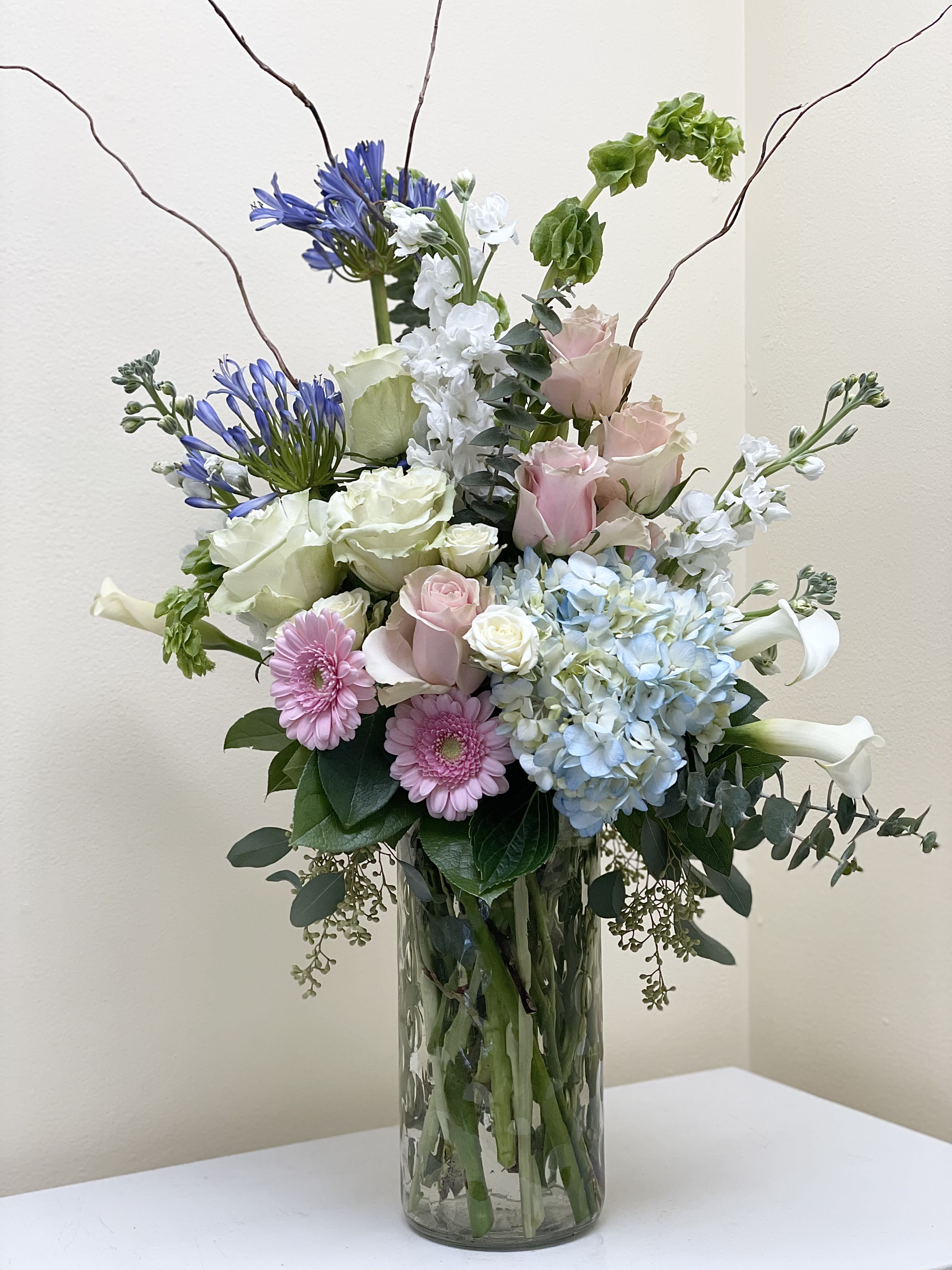 Pastel Sympathy - A tall pastel, beautifully designed arrangement of seasonal blooms and a great collection of greens and textural elements.