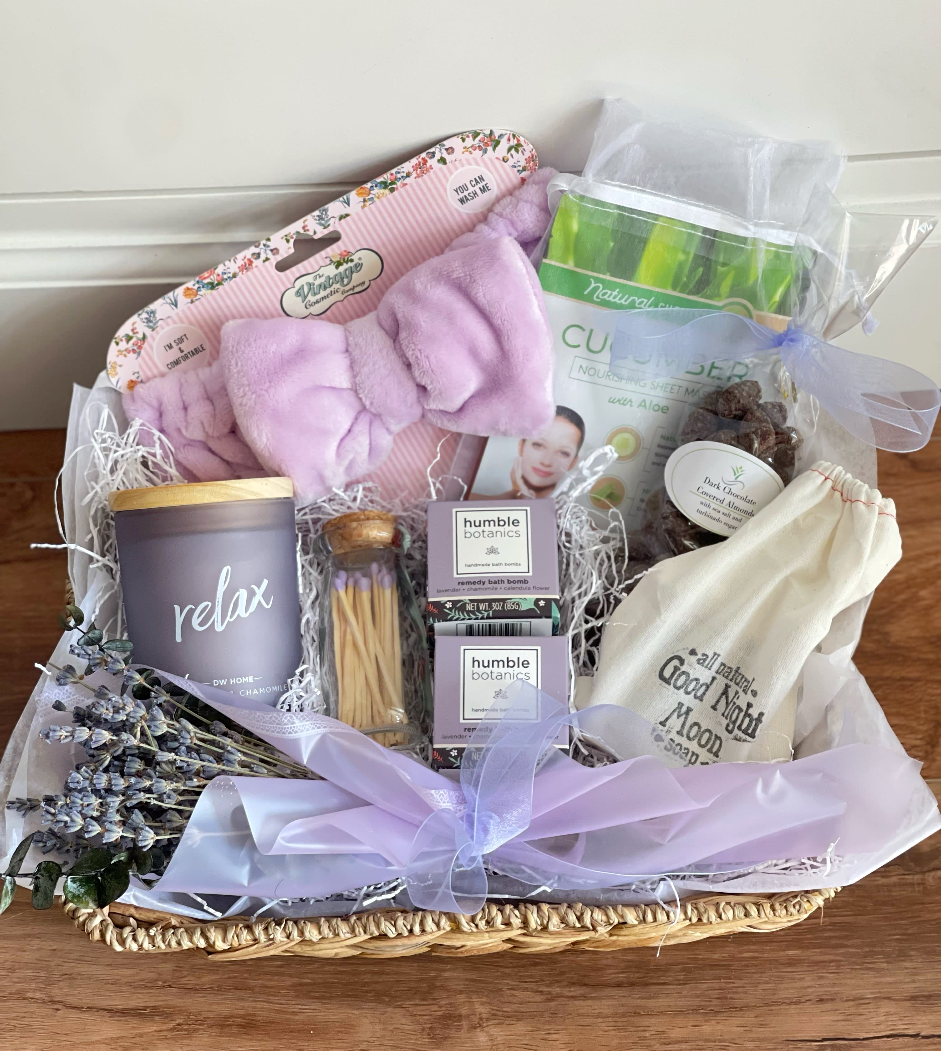 Relax Deluxe  - This gift basket is meant to relax and pamper.  - lavender and camomile candle - Decorative lavender matches in Apothecary Glass Jar, strike paper on bottom of jar. - 2 Humble Botanics Remedy Bath Bombs. Instead of using harmful chemicals, dyes, and fragrances to achieve color and scent, Humble Organics has a non-toxic approach. They use dried calendula flower, and organic lavender and chamomile essential oils. - Naples Soap Company natural Lavender and Patchouli soap - 4 soothing and brightening Korean face masks - soft lavender head band - Dark chocolate covered almonds with sea salt and turbinado sugar - dried lavender bouquet 