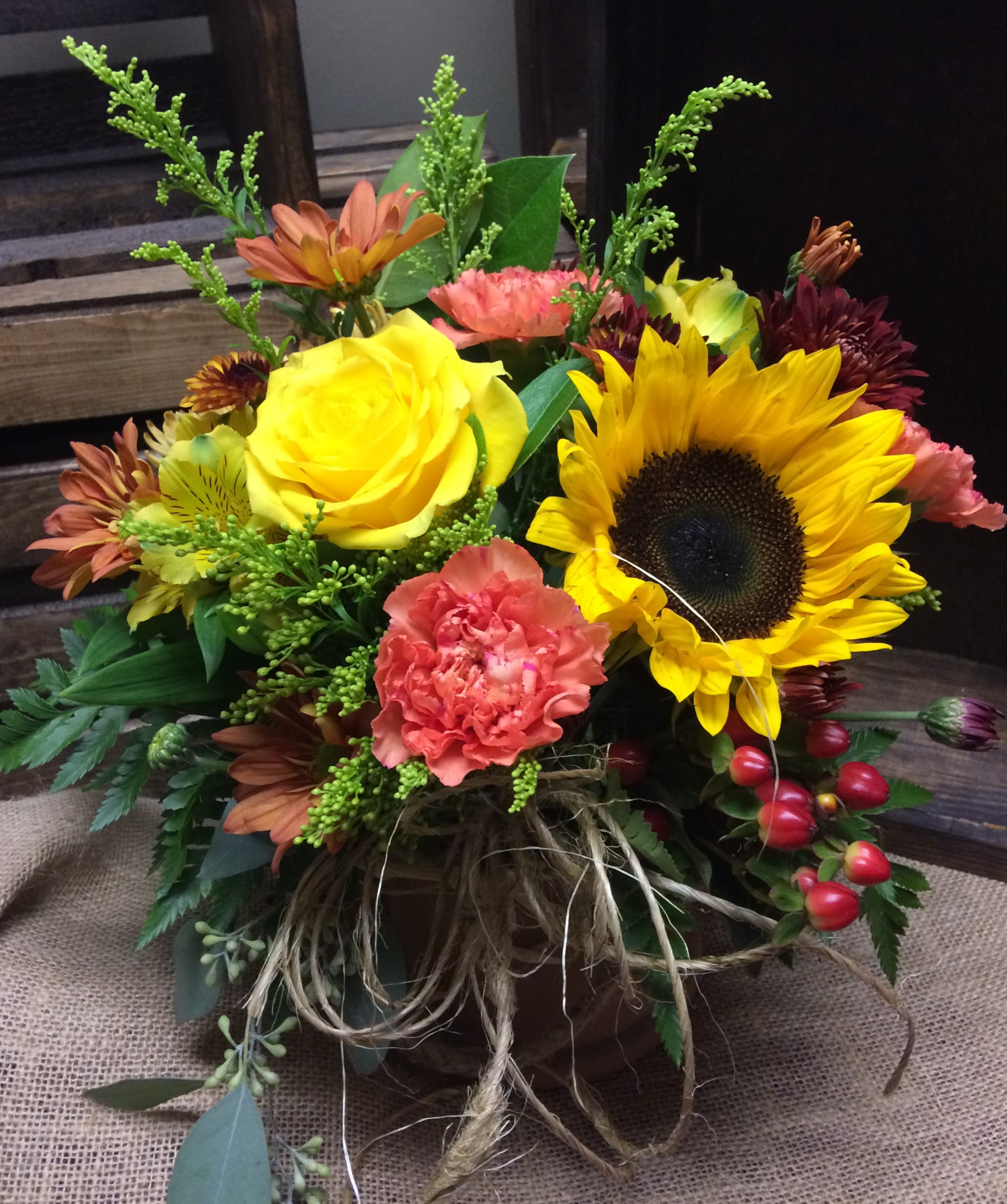 Harvest Time. Custom Design by Cold Spring Floral  - Lower Vased Arrangement with Yellow Roses, Sunflowers, Orange Carnations, Yellow Solidago, Red Hypericum Berry, Yellow Alstroemeria, Rust Colored Mums and  Mixed Greenery with Twine Bow.
