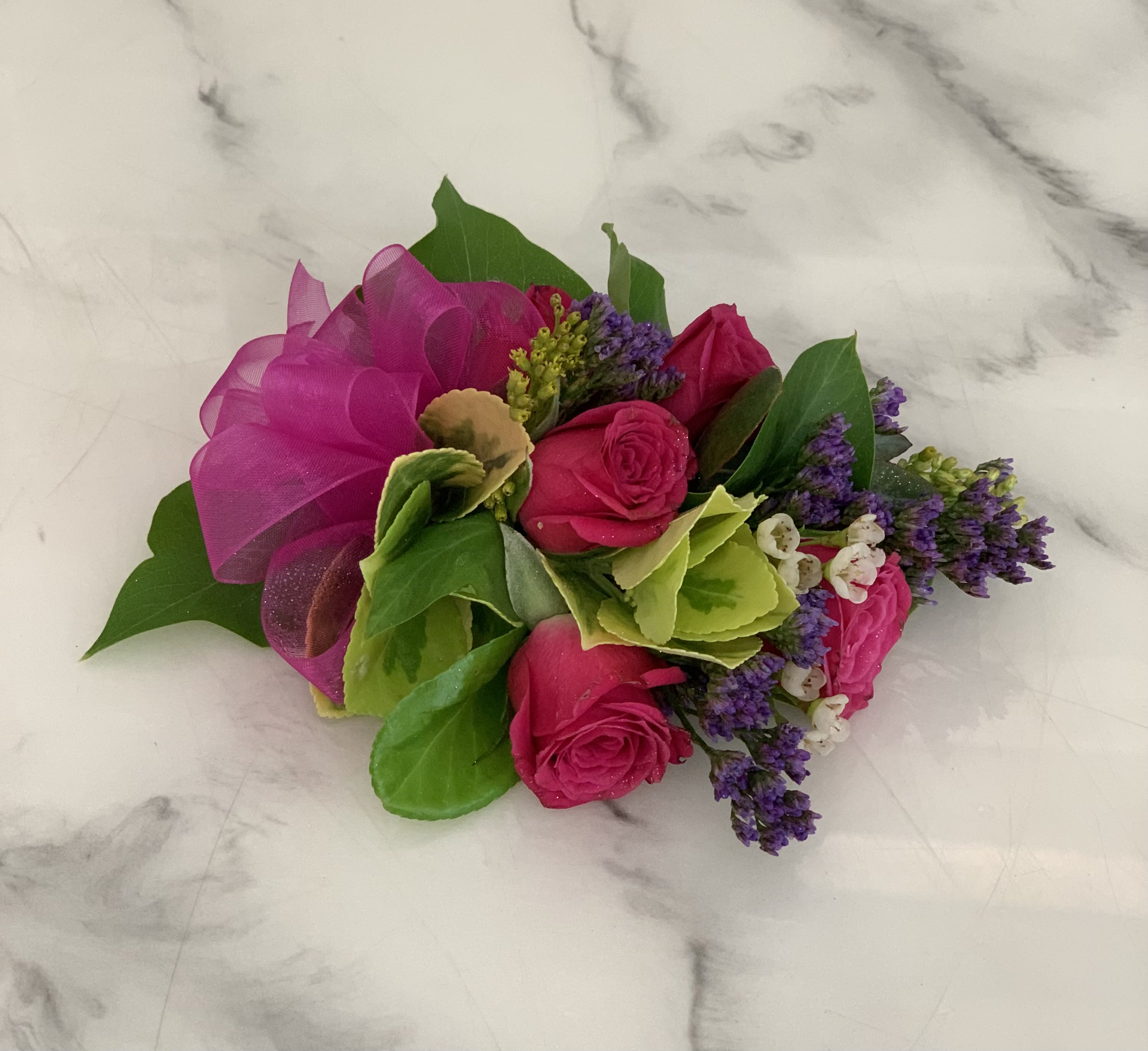 Hot Pink Wrist Corsage Hot Pink Wrist Corsage - A wrist corsage featuring 5 Spray Roses in Hot Pink! Accented with purple, green and yellow filler and foliage. Perfect for a prom or wedding.