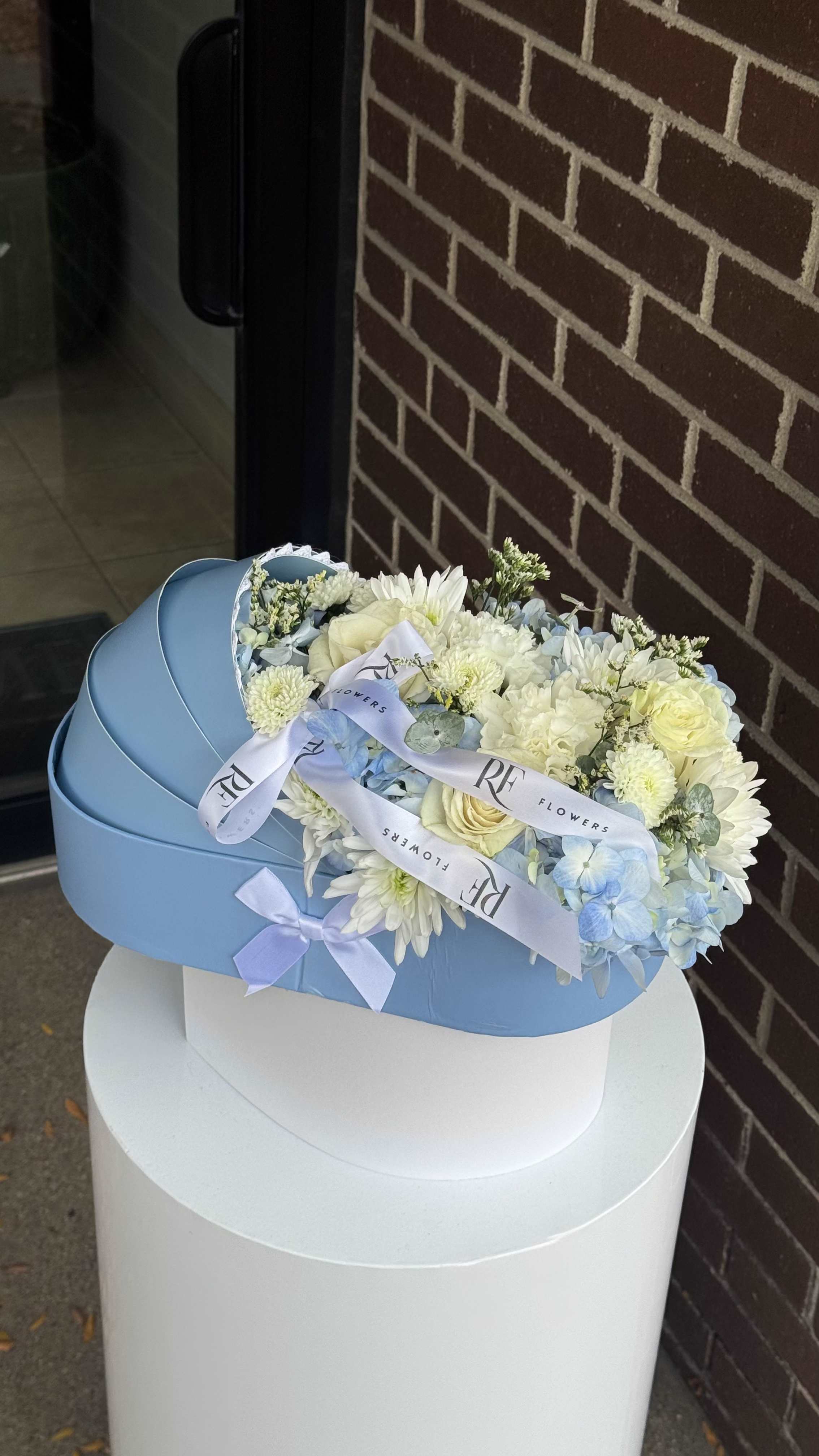 Blue Cradle - A gentle symbol of new beginnings — this tender arrangement celebrates the arrival of a baby boy. Soft white roses and delicate blue blooms are artfully arranged to resemble a tiny cradle, radiating purity, peace, and joy. Perfect for welcoming a newborn and sharing heartfelt congratulations with the family.
