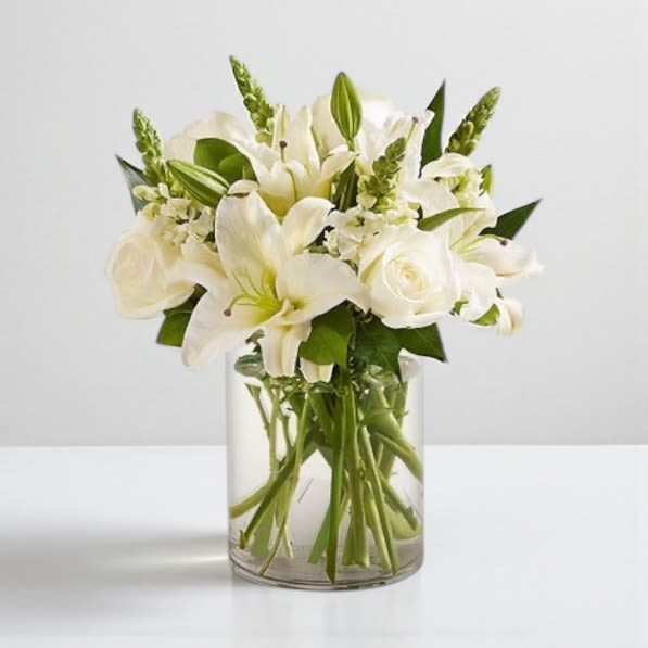 Timeless White Elegance - White flowers symbolize grace, purity, and serenity, making this elegant arrangement perfect for any occasion. Whether celebrating a special moment, expressing gratitude, or offering comfort, this beautifully crafted design brings a sense of peace and sophistication. Hand-gathered by our expert florists with lush greenery, it’s a timeless gift that conveys your sentiments with elegance.  Details: Floral Selection: White roses, lilies, and snapdragons, complemented by fresh greenery Vase: Arranged in a classic glass cylinder vase (8&quot;H) Available Sizes: Ultra Premium: Approximately 21&quot;H x 21&quot;W Premium: Approximately 20&quot;H x 20&quot;W Deluxe: Approximately 19&quot;H x 16&quot;W Standard: Approximately 18&quot;H x 14&quot; W Additional Notes:  To ensure lasting beauty, lilies may arrive in bud form and will fully bloom in a few days Can be sent to the funeral service or the home. Colors, varieties and container may vary due to local availability A versatile gift suitable for celebrations, sympathy, or simply to brighten someone’s day  This classic white floral arrangement is a timeless expression of elegance, making it a meaningful gift for any occasion.