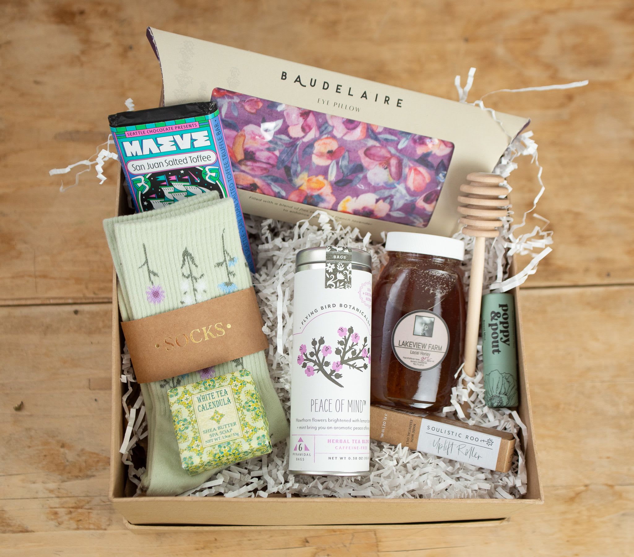 The Comfort Kit Gift Box - A little box of calm, crafted to lift your spirits and wrap you in cozy comfort. Inside you’ll find floral socks to warm your toes, a soothing eye pillow to ease the day away, and a blend of thoughtful treats—like herbal tea, honey, and chocolate—to bring simple joy to your senses. With mood-boosting aromatherapy, soft lip gloss, and a beautifully scented soap, this kit is your gentle reminder to pause, breathe, and take care.  Perfect for a friend in need of a pick-me-up—or for yourself, because you deserve it.  **If an item is unavailable we will substitute with a similar item of equal or greater value.