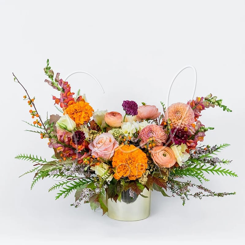 Autumn Sunset - Bring the rich beauty of fall indoors with our Autumn Sunset arrangement. This seasonal design features a warm blend of orange marigolds, blush roses, peach ranunculus, burgundy scabiosa, and sunset snapdragons, paired with lush greenery and autumn berries.  Arranged in a modern gold vase 4&quot;, it's perfect as a Thanksgiving centerpiece, a fall gift, or elegant seasonal décor. Handcrafted by our expert florists, Autumn Sunset captures the magic of autumn in every detail.