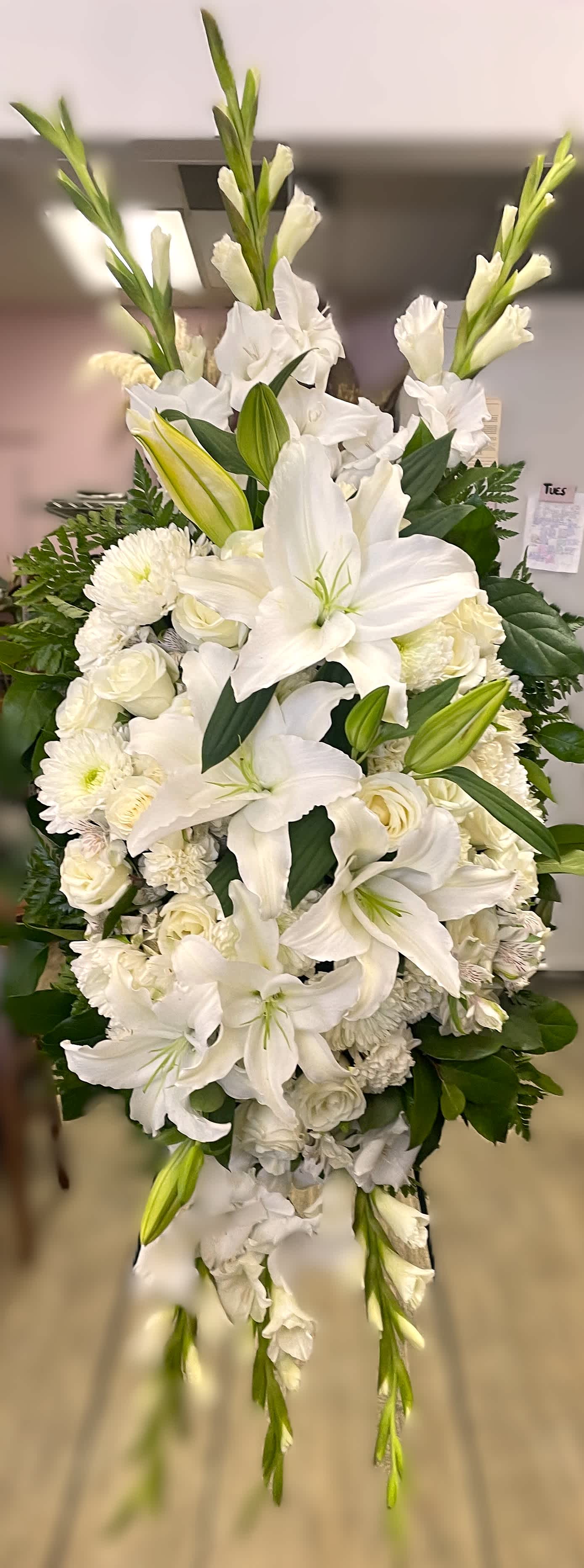 Peaceful Embrace Standing Spray Peaceful Embrace Standing Spray - A serenely beautiful standing spray that is approximately 54" tall and 28-32" wide. It is a lovely tribute for any service. Made of white lilies, white roses, white carnations, white mums, greens and white gladiolus, and greens. Includes the easel for the spray.