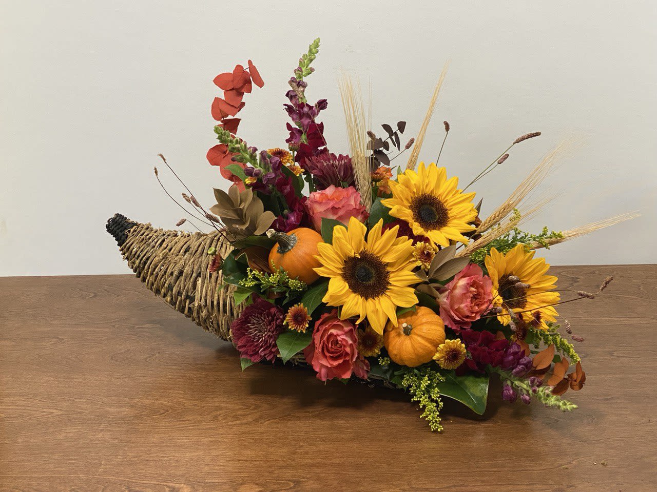Golden Harvest Cornucopia Golden Harvest Cornucopia - Celebrate the abundance of the season with our Golden Harvest Cornucopia — a stunning centerpiece overflowing with fall’s natural beauty. Sunflowers, roses, chrysanthemums, and snapdragons mingle with miniature pumpkins, golden wheat, and autumn foliage, all artfully arranged in a woven horn of plenty. Perfect for Thanksgiving tables, seasonal gatherings, or as a warm gift of gratitude, this arrangement captures the spirit of harvest and the cozy charm of autumn.