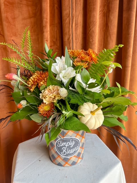 Simply Blessed Simply Blessed - A cheerful mix of fall blooms and fresh greenery designed in our seasonal “Simply Blessed” ceramic container. Featuring warm orange tones, creamy whites, lush greens, and a touch of harvest texture — complete with a mini pumpkin accent. Perfect for expressing gratitude or brightening any space this autumn. Container design may vary slightly based on availability.