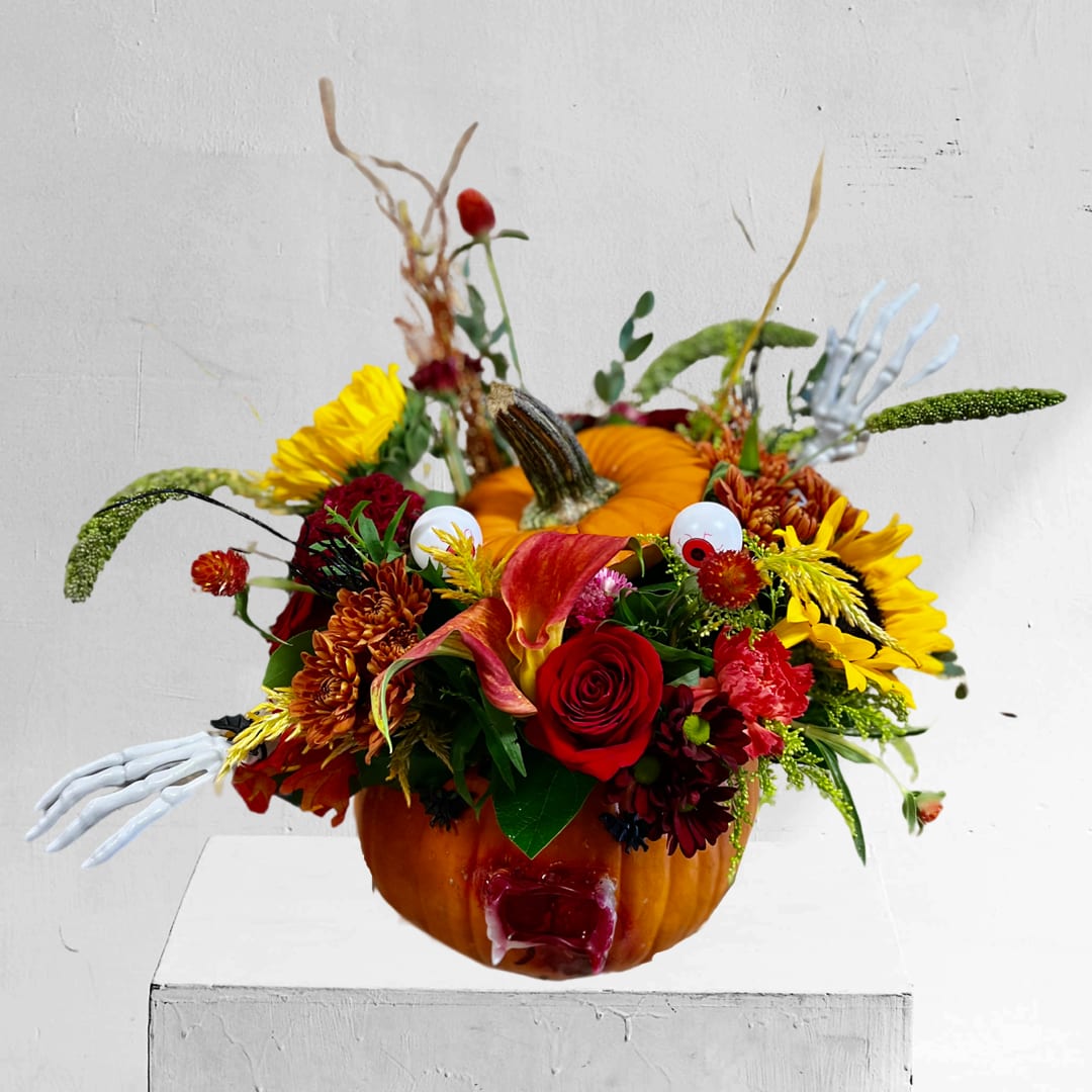 Spook-tacular in Natural Pumpkin - Type Of Flowers: Red Roses, Black Calla Lilies, Sunflowers, Red Carnations, Brown Cushion Pom Poms, with a grueling face on a Natural Pumpkin and more! Availability: All year round Substitute Available: Yes Design View: Asymmetric Front Facing View Photo shown: Regular