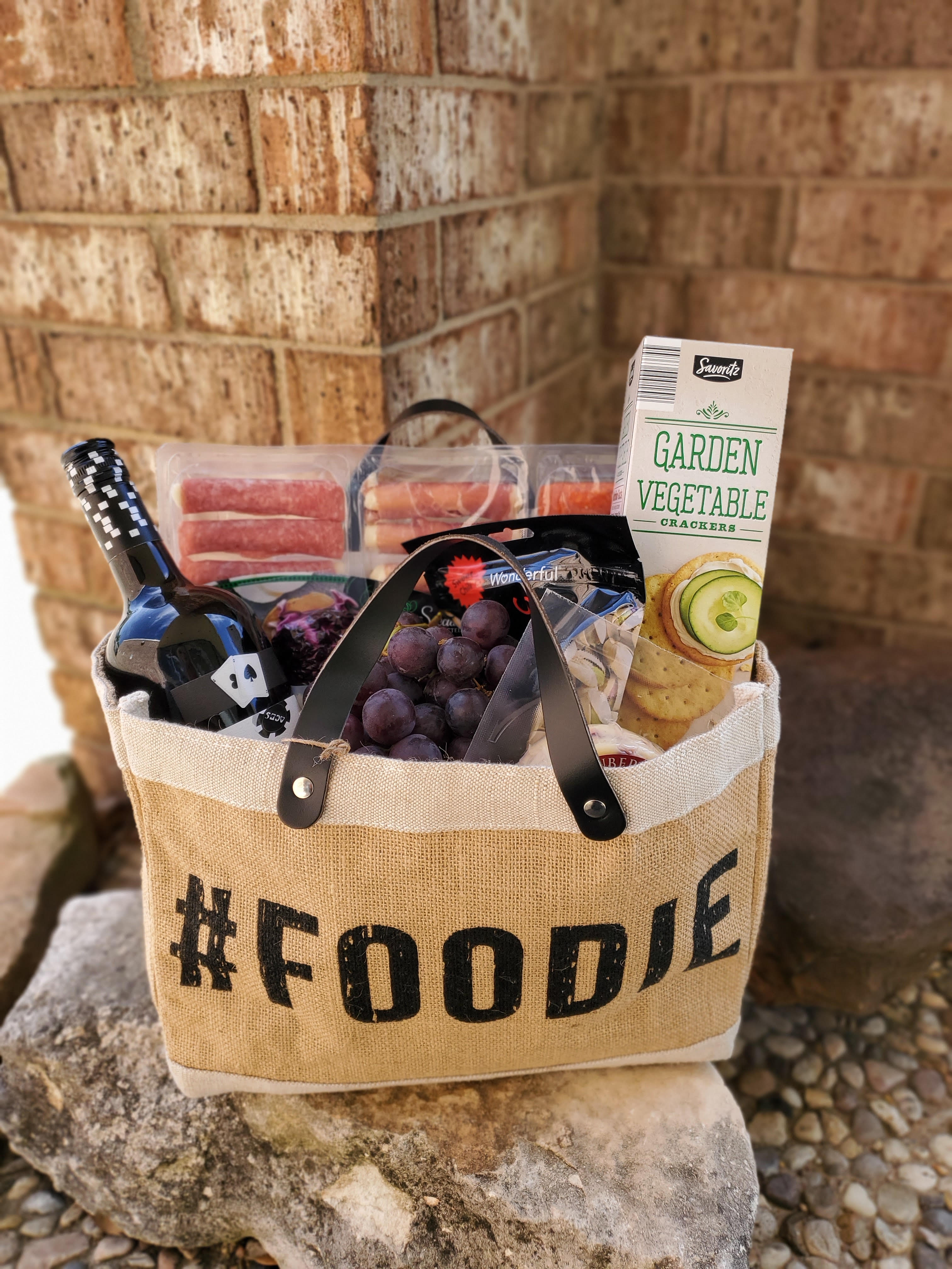 Foodie Basket Foodie Basket - ***THIS PRODUCT REQUIRES 24 HOUR NOTICE ***  Our version of a charcuterie spread, including a bottle of wine and a variety of cured meats, cheeses, fruits, crackers and nuts in our re-useable #FOODIE Bag.  **IMPORTANT INFO: Orders containing alcohol must be purchased by individuals over the age of 21, or of legal drinking age in your area. Delivery MUST be within our serviced area and must be accepted by an individual over 21 with valid ID. Deliveries can not be delivered to areas where consumption is prohibited (business offices, campus dorms, etc.).