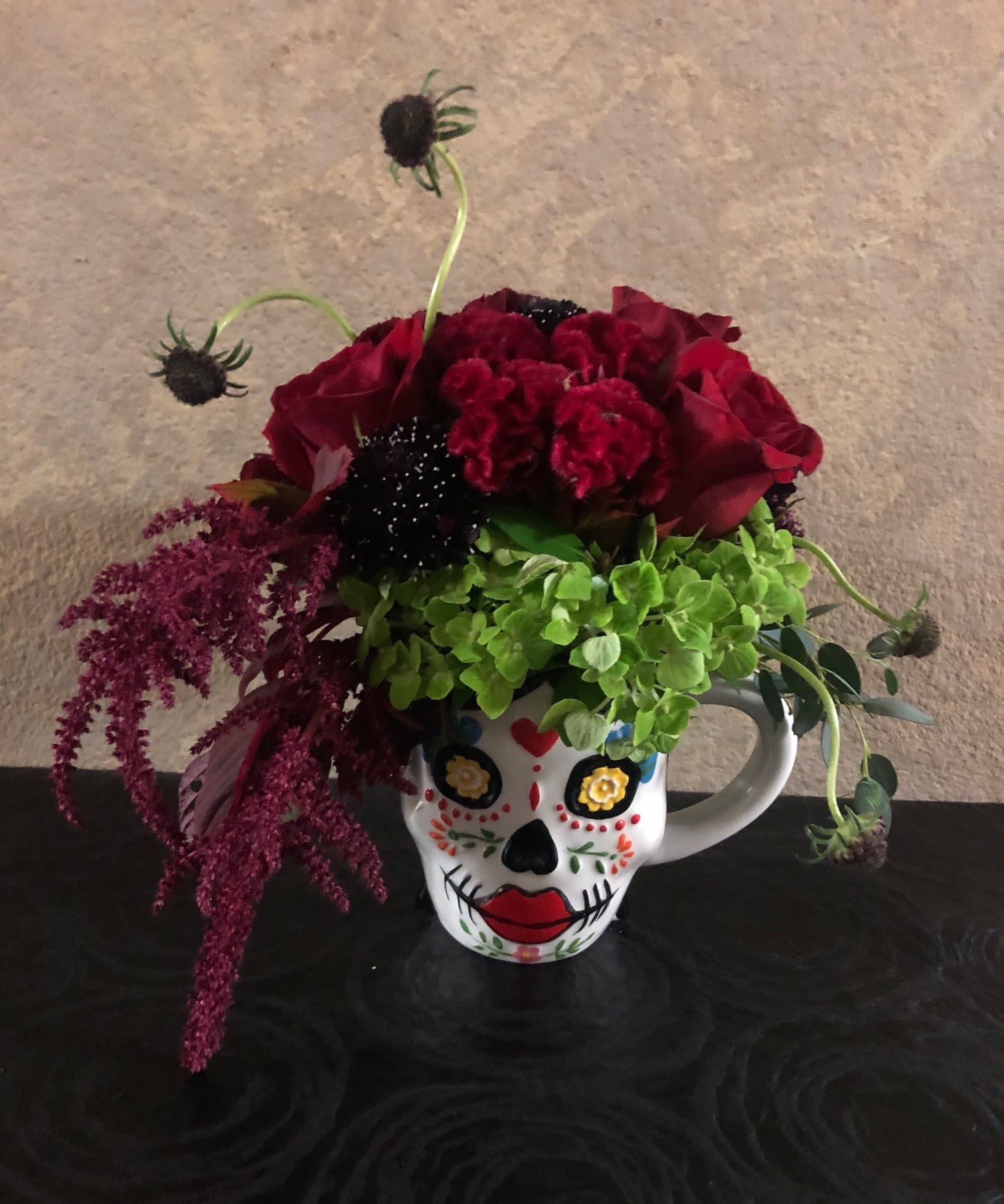La Catrina La Catrina - Type of Flowers: Red roses, Green Hydrangeas, Scabiosa, Amaranthus Caudatus, Celosia Cockscomb in a coffee mug. Availability: Limited coffee mug available. Substitute Available: Yes Design View: All Facing View Photo shown: Regular