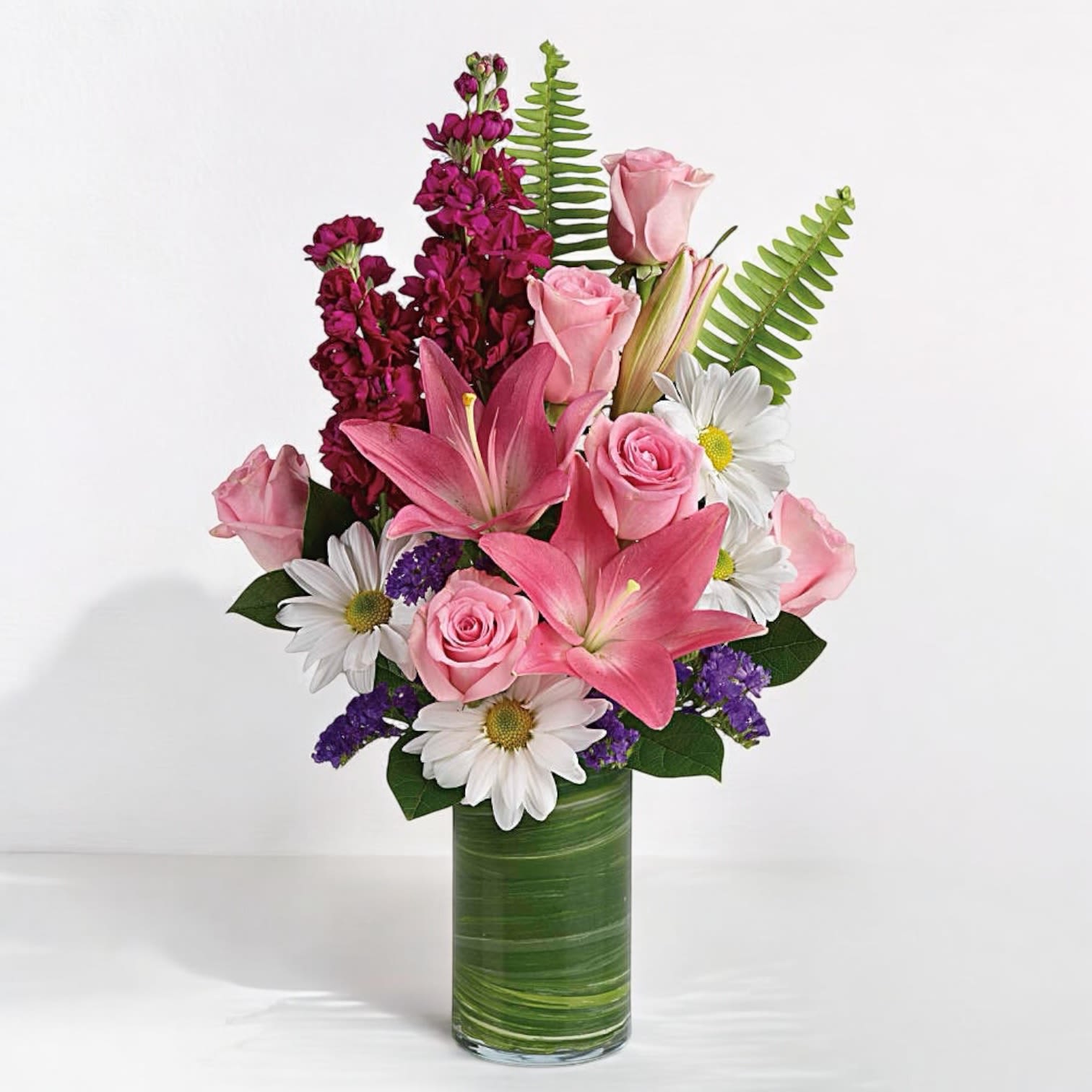 Playful Daisy Bouquet - Bring a touch of joy and happiness into any space with our cheerful floral bouquet. Full of whimsy, this Playful Daisy Bouquet of pink roses, white daisies, pink lilies and fuchsia stock is a fun surprise for any special occasion! It's wrapped in a ti leaf in a glass cylinder vase for a modern touch.&nbsp;  Pink asiatic lilies, pink roses, fuchsia stock, white daisy spray chrysanthemums, and raspberry sinuata statice are accented with sword fern, variegated ti leaf, and lemon leaf. Delivered in Clear Glass Cylinder vase. Orientation: All-Around  Sizes  Standard: 18 1/2&quot; H x 11 1/2&quot; W Deluxe: 18 1/2&quot; H x 11 1/2&quot; W Premium: 18 1/2&quot; H x 11 1/2&quot; W    &nbsp;  