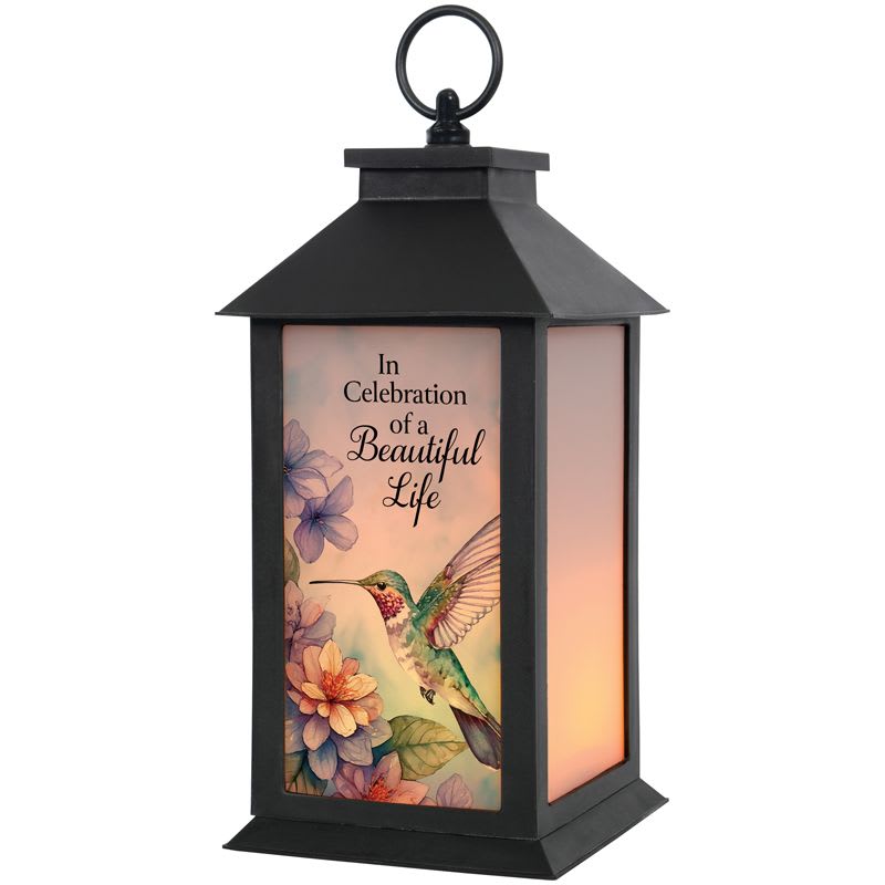 Beautiful Life Lighted Frosted Lantern Beautiful Life Lighted Frosted Lantern - This light up lantern has frosted glass and features a hummingbird scene with the saying, "In Celebration of a Beautiful Life". These lanterns are made of weather friendly materials and UV printed frosted glass. They include a flameless LED candle with a built-in automatic timer: 6hrs ON/18hrs OFF (3 AAA batteries are included). They are suitable for hanging or free-standing use. Comes with a bow to match the lantern. W: 5.5" H: 13" D: 5.5"