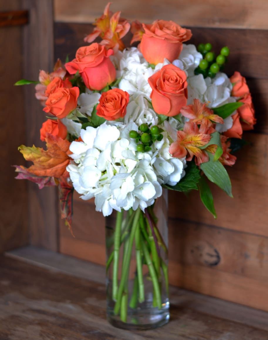 Seasonal Serenade - This beautiful Seasonal Serenade is designed in a 9” cylinder vase and packed with White Hydrangeas, Orange Roses, Orange Spray Roses, Orange Alstroemeria, Green Hypericum and Synthetic Seasonal Leaves. This arrangement is available in three different pricing variations to which our designers will fill to value with more roses and seasonal flowers. Seasonal Serenade is a beautiful bouquet that is appropriate for any occasion this Autumn. 