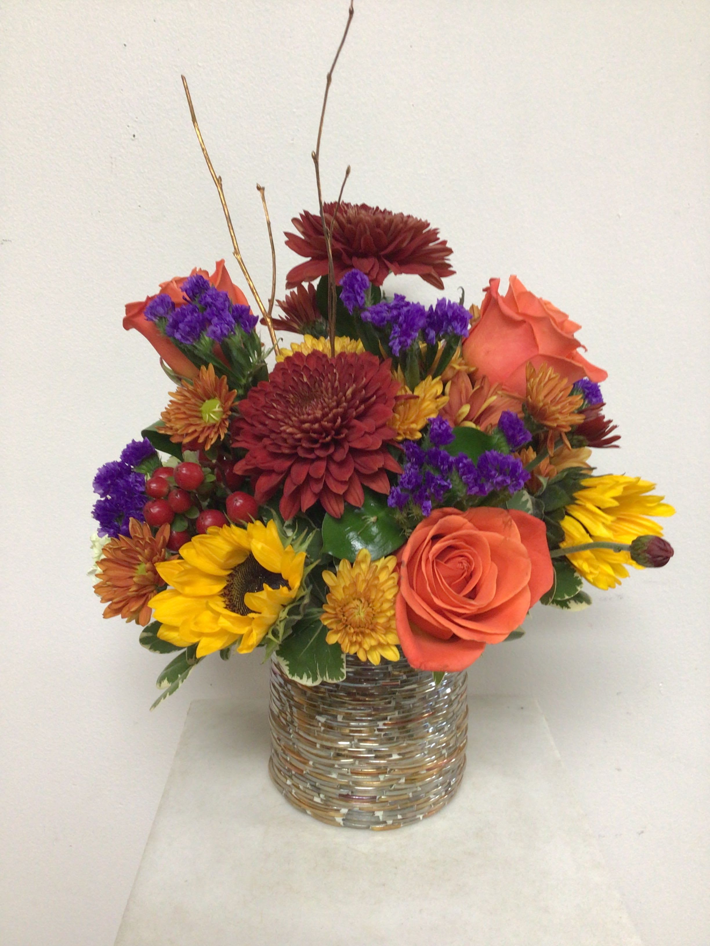 Joyful Fall Joyful Fall - 5 inch cylinder embossed with a basket weave design and arranged with orange roses, sunflowers, mahogany hypericum berries, purple statice mini green hydrangea, and a variety of colorful fall mums. This arrangement is all around and approximate size is 14 inches tall by 11inches wide.