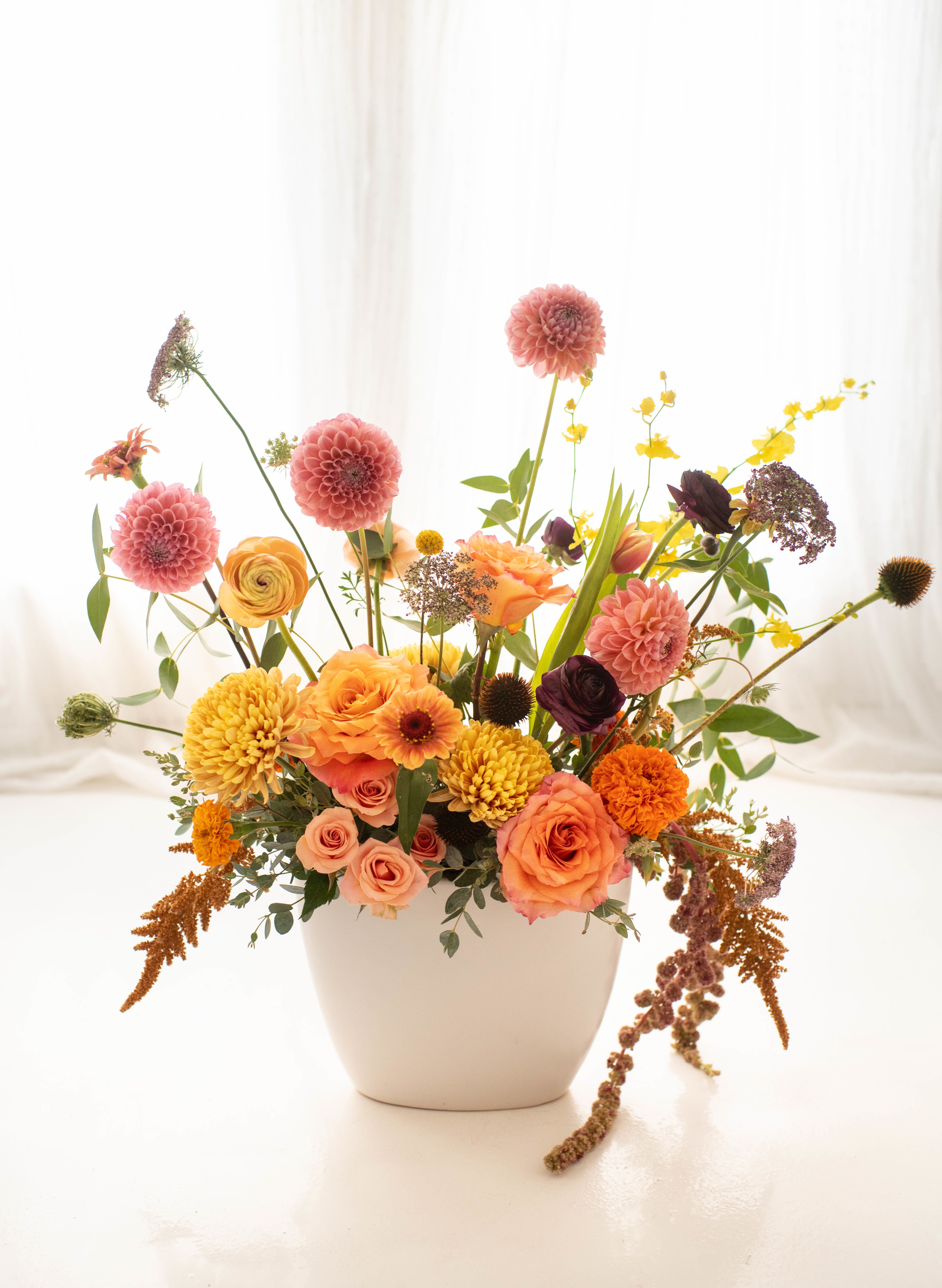 Fall Grace - A striking blend of premium fall blooms artfully arranged in a sleek white ceramic vase, approximately 22&quot; tall. While the flowers may vary from the image, you can expect a beautiful arrangement that elevates any space.  