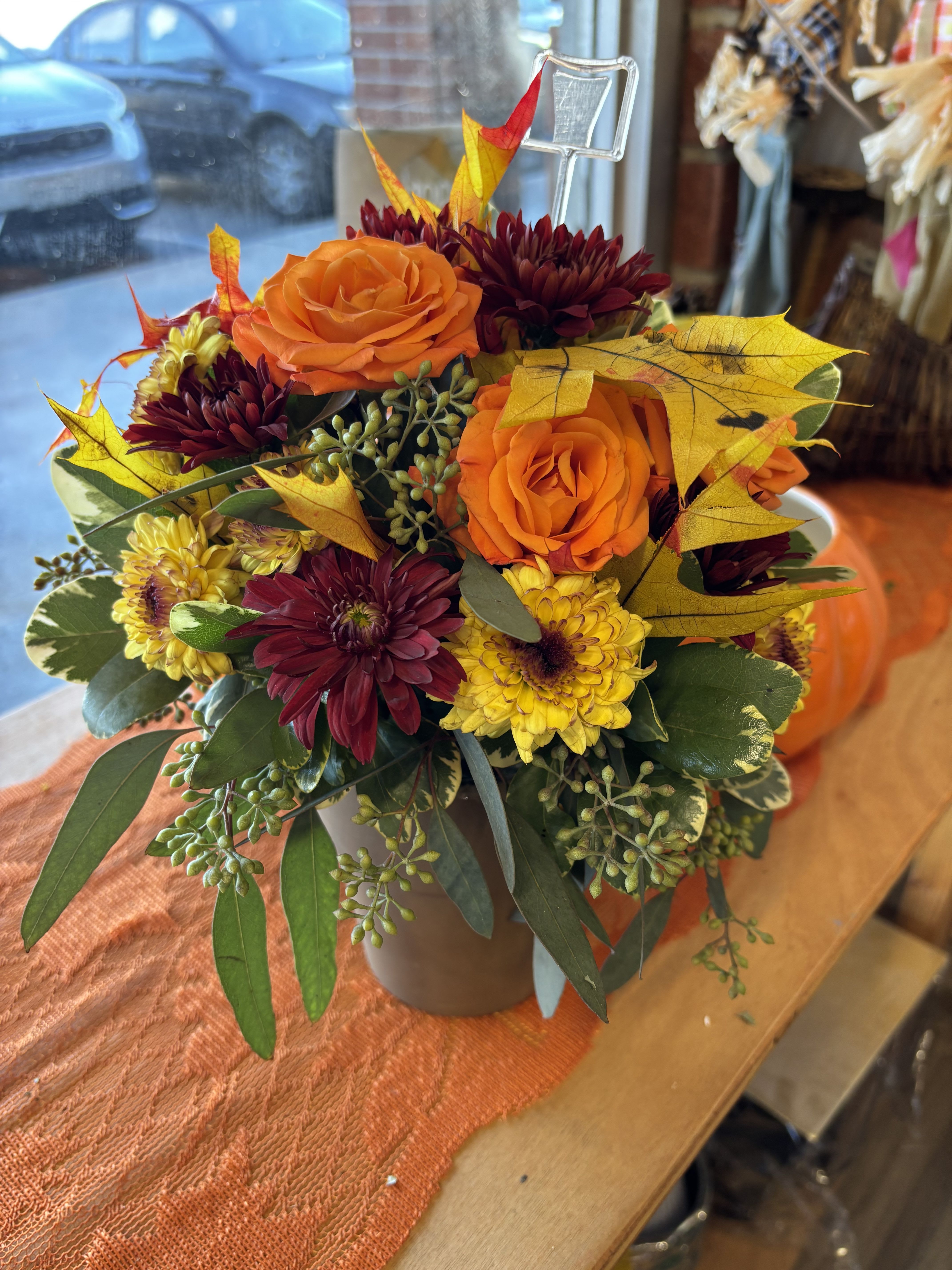 Sugar Maples Sugar Maples - Autumnal colors of yellow, bronze and green - set off by fiery orange roses, seeded eucalyptus and hypericum - nestle together with brilliant fall leaves to create a bright floral arrangement that's reminiscent of a walk in the woods at sugar maple time. A pot adds a rustic touch.   SUBSTITUTION POLICY Always deliver the freshest flowers! Please note the bouquet pictured reflects our original design.  If the exact flowers or container in this arrangement are not available, our local florists will create a beautiful bouquet with the freshest available flowers.
