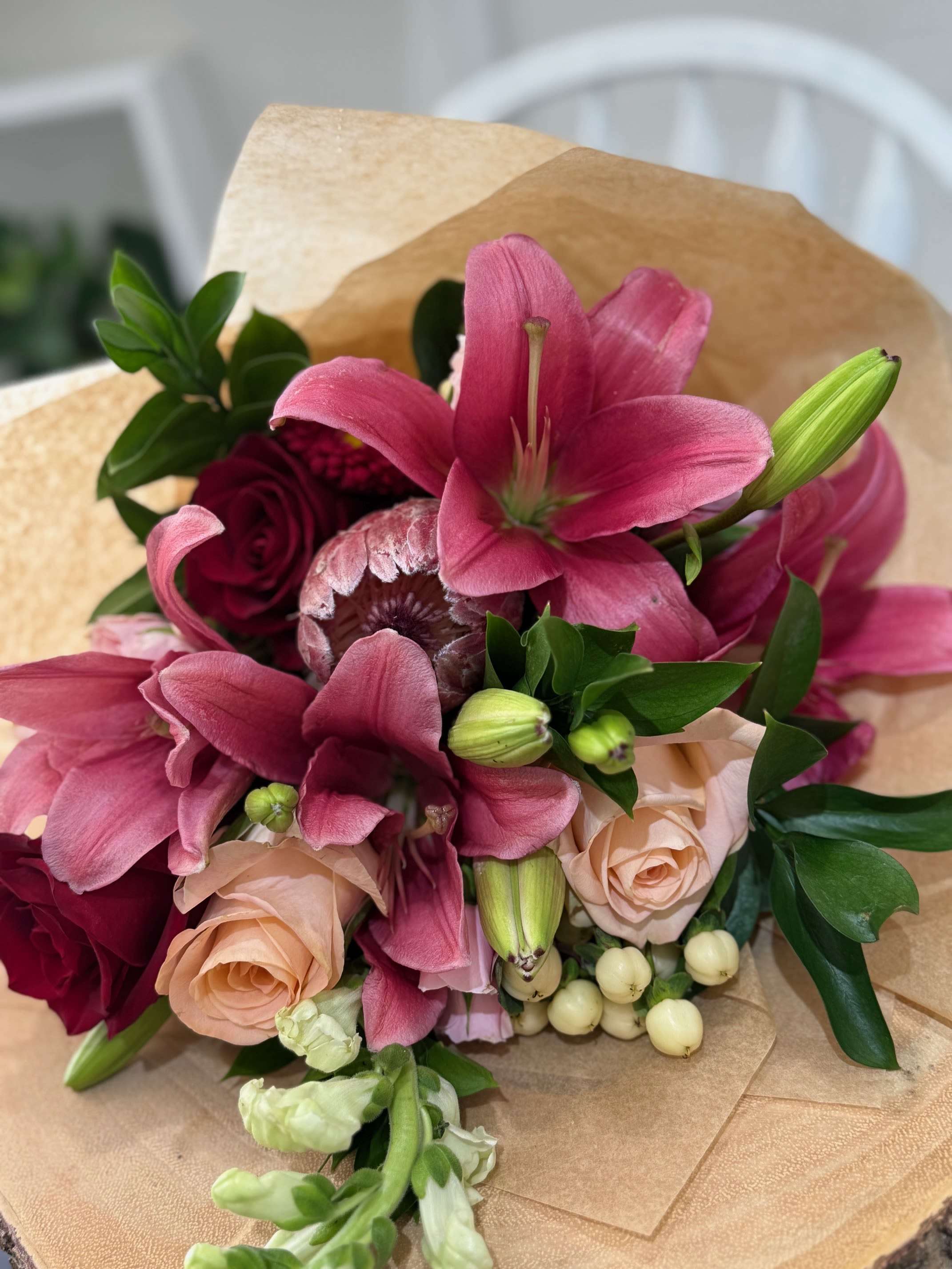 The Ever After  Bouquet - A breathtaking mix of two king proteas, classic lilies, and elegant roses, artfully wrapped for a natural, romantic feel. Designed to impress and delivered with a clear glass vase for easy display.