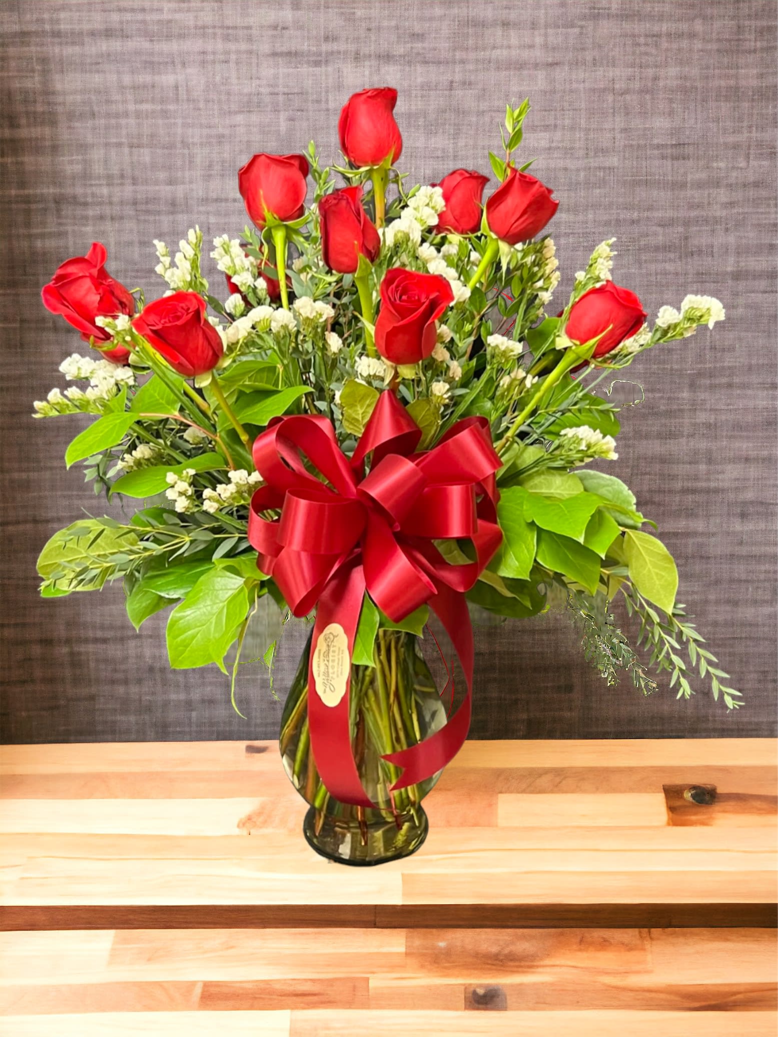 Dozen of Love - Share the love 12 times over with our beautiful red roses.  Standard shown, Designed in a clear glass vase with three different types of greenery and filler.