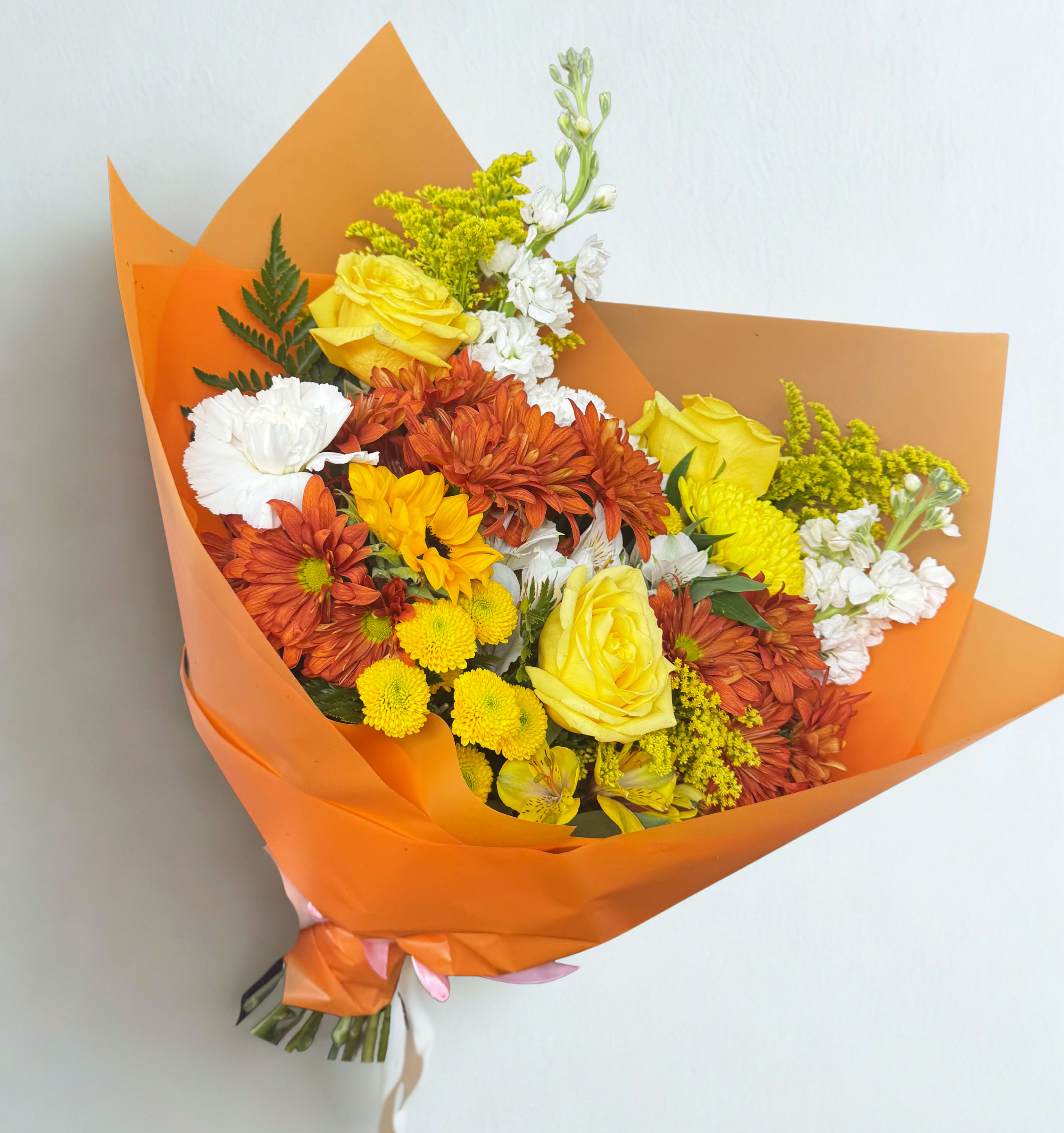 Golden Glow Golden Glow - A warm and vibrant bouquet inspired by autumn sunsets. Featuring yellow roses, chrysanthemums, white carnations, alstroemeria, and solidago, wrapped in bold orange paper. Perfect for brightening someone’s day or celebrating new beginnings. Note: Some flowers may be substituted with equal value seasonal blooms for freshness and quality.