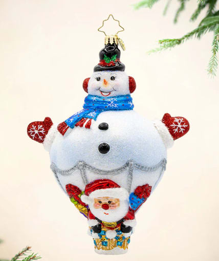 Radko Up, Up & Snowy Radko Up, Up & Snowy - Soar through the skies on a snowy adventure with our Up, Up, and Snowy ornament. This charming piece features a friendly snowman hot-air balloon, and a jolly Santa Claus ready to embark on a festive flight.
