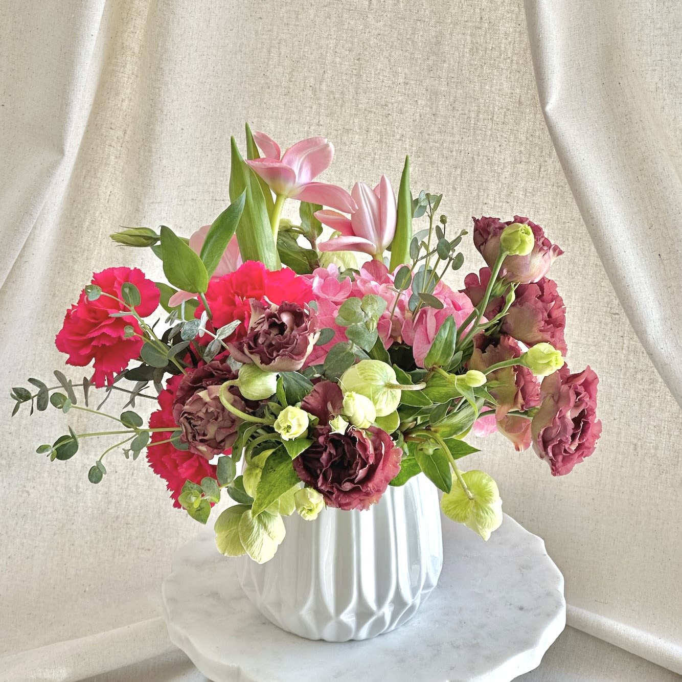 Guava  - Hot pink, brown, and green flowers arranged in a white ceramic vase.   Flower types may vary depending on the season.