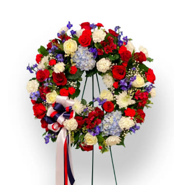 Sympathy Collection Standing Wreath - Thank You for Your Service Tribute  - Red, white and blue wreath symbolizing eternal life and honoring service in a U.S. military.  A beautiful combination of roses, hydrangea, mums, and accent flowers  - with a tri-colored bow. A lovely piece for a memorial service, celebration of life service or Memorial Day of Veterens Day tribute or remembrance. Truly a stunning design. 