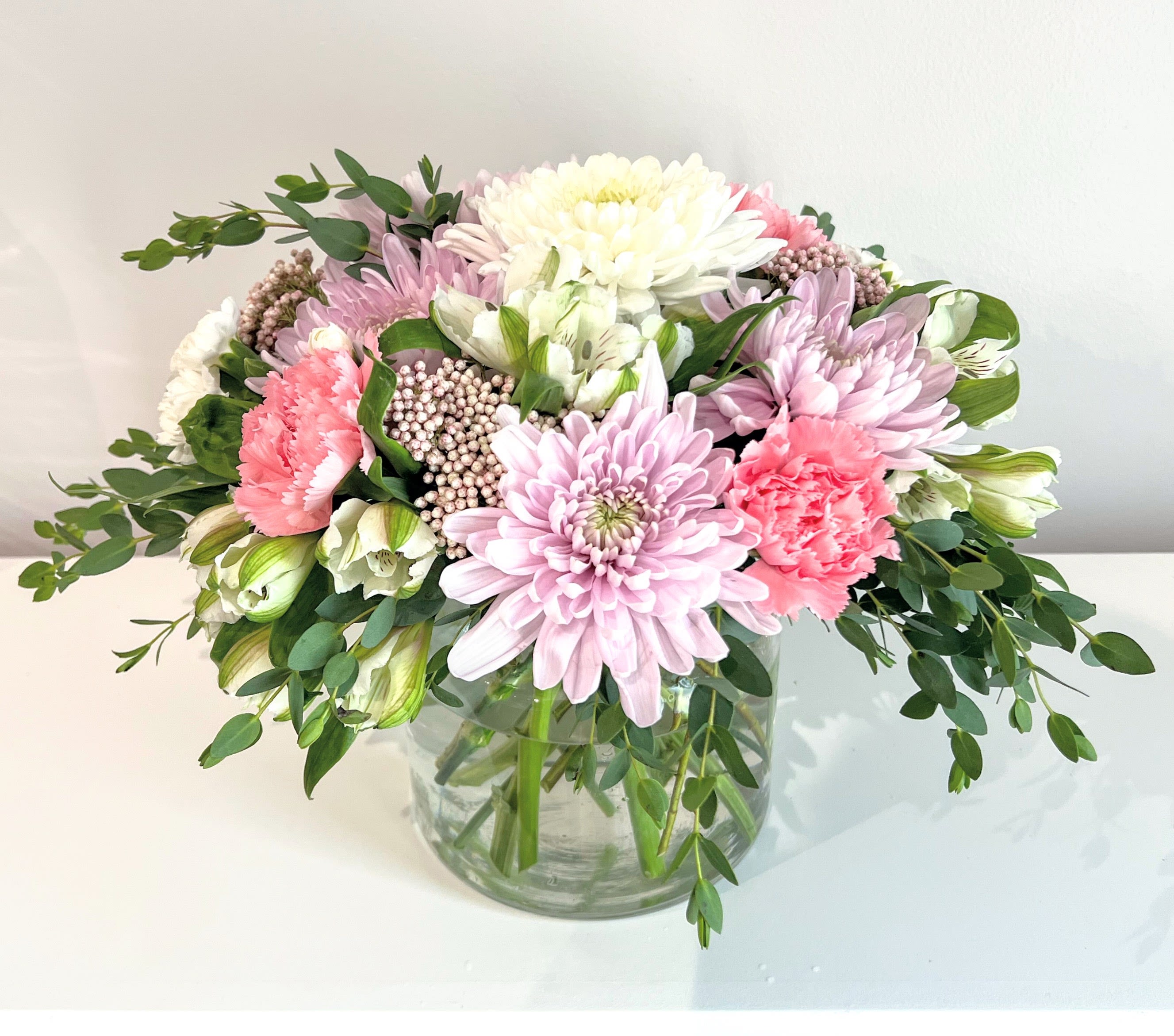Country Garden Country Garden - A fresh pastel colored floral bouquet featuring the freshest seasonal blooms in white, lavender & pink, Large long lasting flowers like large dish bud mums, carnations, rice flower, alstroemeria & fragrant eucalyptus greens are arranged low & compact in a classic clear glass cylinder. Perfect for Mother's Day or any special occasion. Measures: approx. 11" tall & 11" wide Orientation: All around