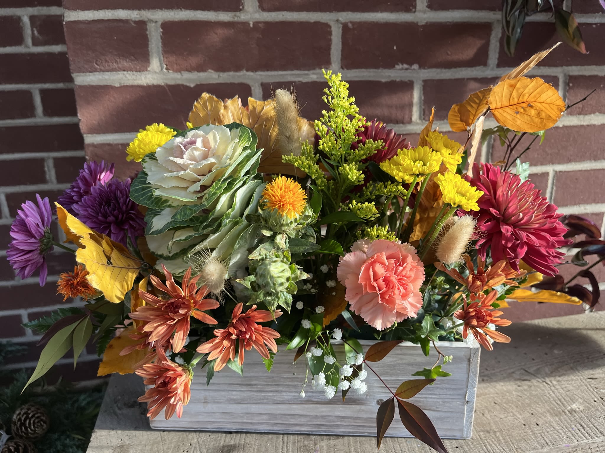 Thanksgiving Centerpiece Thanksgiving Centerpiece - A colorful centerpiece for Thanksgiving dinner.  The 4x8x4 inch wood box is filled to the brim with leaves, grasses, and flowers.  Mums and ornamental Kale take center stage with this arrangement.  Order for delivery or pick-up at my studio in Reisterstown or at The Boxwood Collection in Glyndon, The Reister's Daughter in Reisterstown, or Redemption Springs in Finksburg.  If you would like to pick up the arrangement at someplace other than my studio please choose studio pick-up and indicate the place of pick-up in the notes section (yes delivery is free to these wonderful stores!).    If you would like a longer or larger arrangement than is offered here please contact me for a custom arrangement.