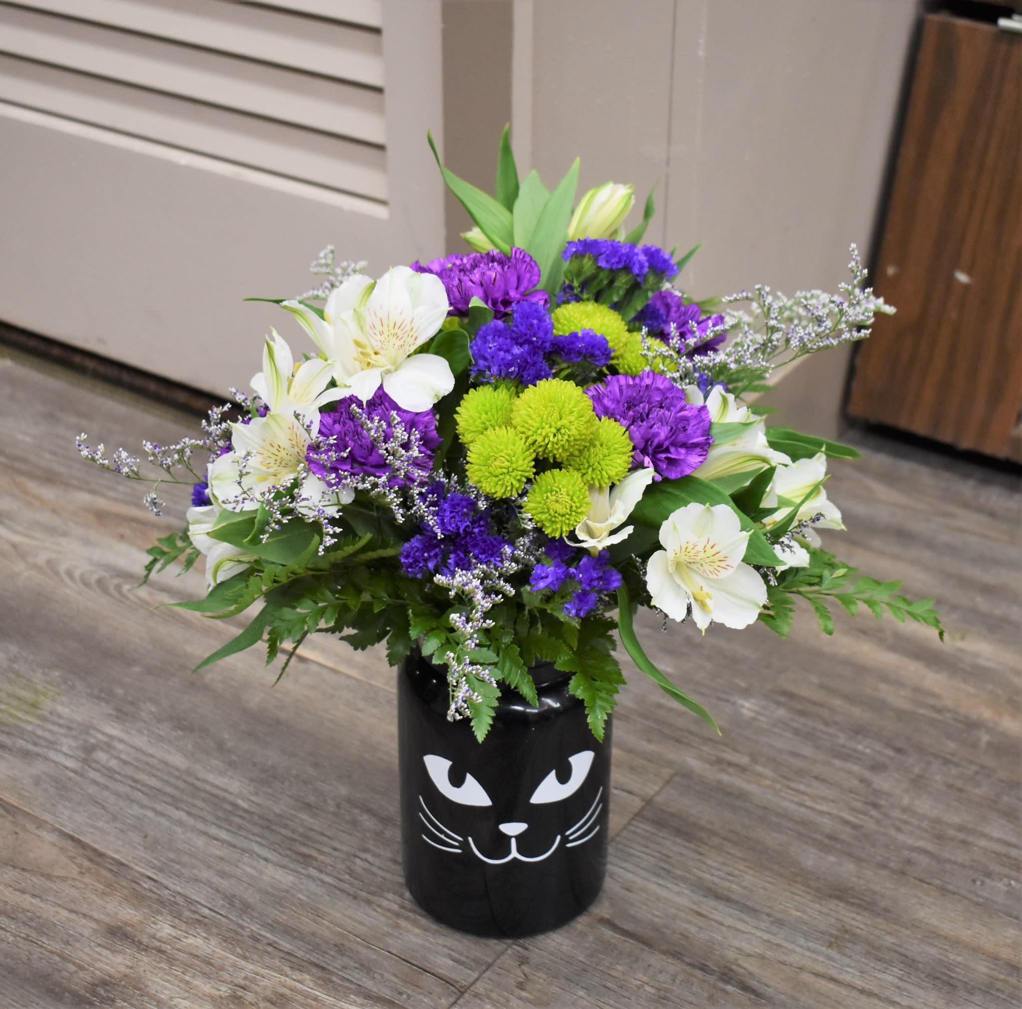 Salem Salem - Superstition says that a black cat crossing your path is bad luck...but this adorable vase will be sure to brighten anyone's day! White Alstromeria, purple carnations, green button mums, purple status, caspia and fresh greens are designed in a glass cat vase...the perfect way to celebrate spooky season!