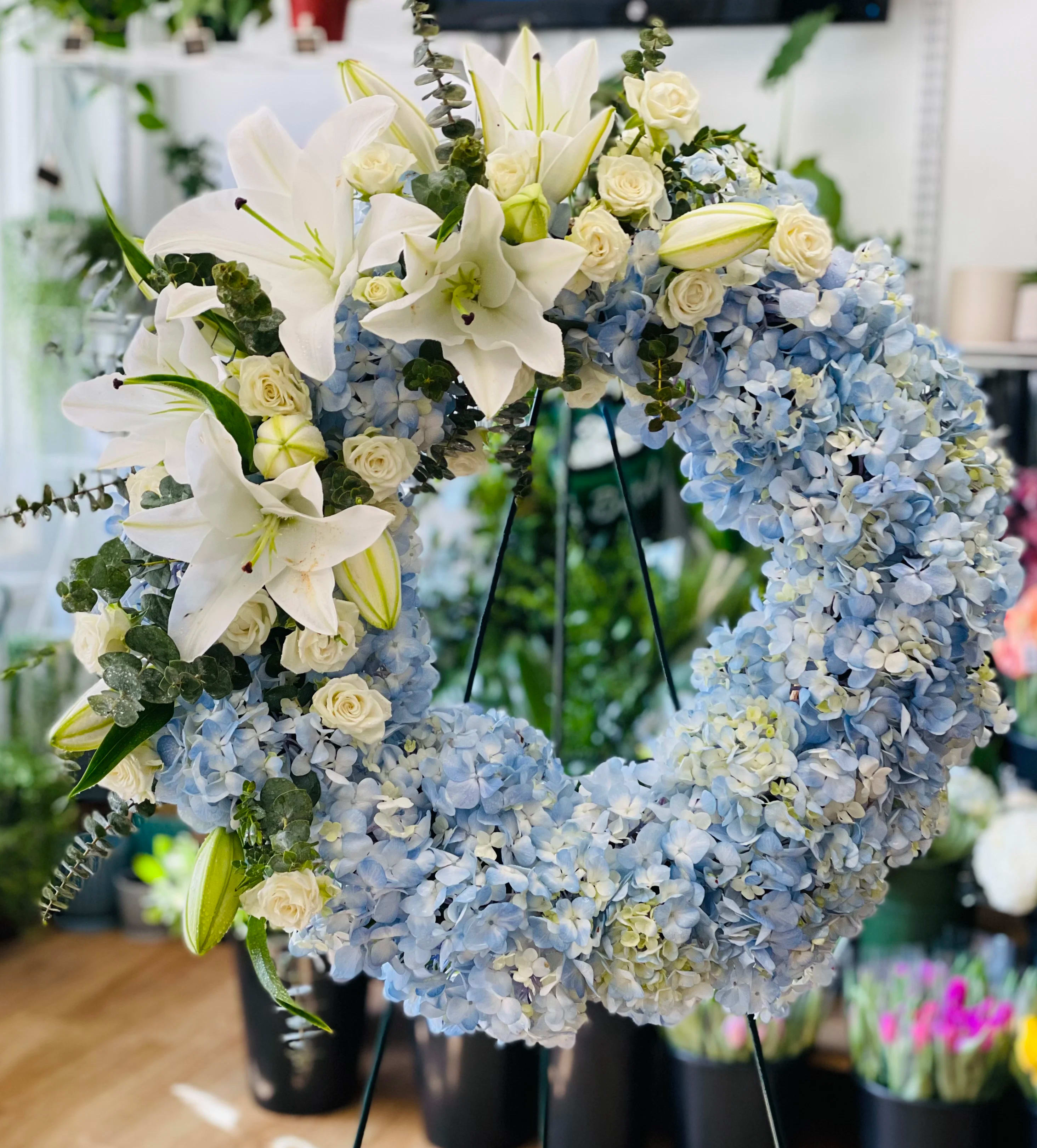 Blue and White Wreath Blue and White Wreath - Foliage includes: Lily, Spray Rose, Hydrangea and Baby Blue Eucalyptus   We advise our customers to order 24-48 hours in advance of their scheduled delivery to ensure that we are able to have similar flowers and colors in the shop for their order.  $250 (18 inches) as shown