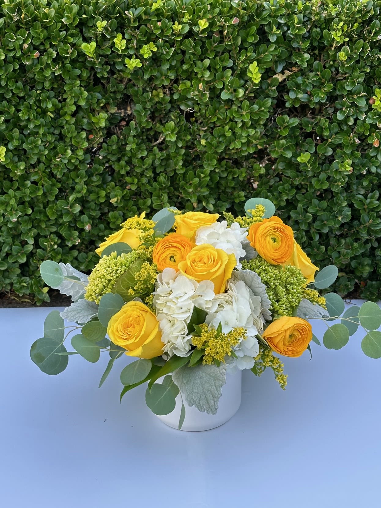 Here Comes the Sun Here Comes the Sun - Brighten the day with this sunny fresh floral gift featuring yellow roses, white hydrangea and yellow ranunculus artfully designed in a ceramic white pot.