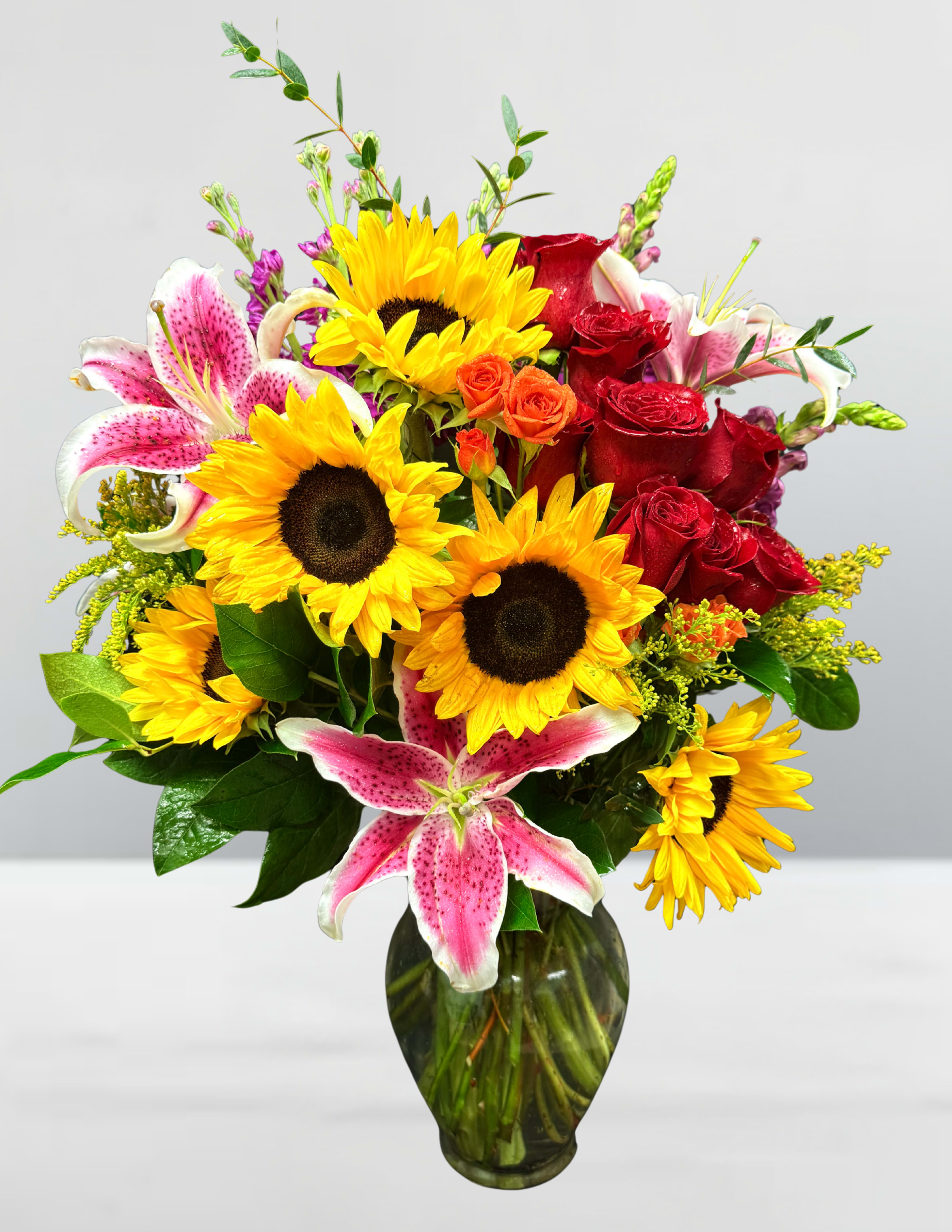 Floral confetti - Floral Confetti A joyful burst of color that feels like a celebration in bloom! Sunflowers beam with golden cheer, stargazer lilies dazzle with speckled flair, and roses in fiery red and orange dance among sprigs of yellow solidago and lush greenery. This bouquet is pure happiness—like tossing petals into the air and watching smiles bloom.