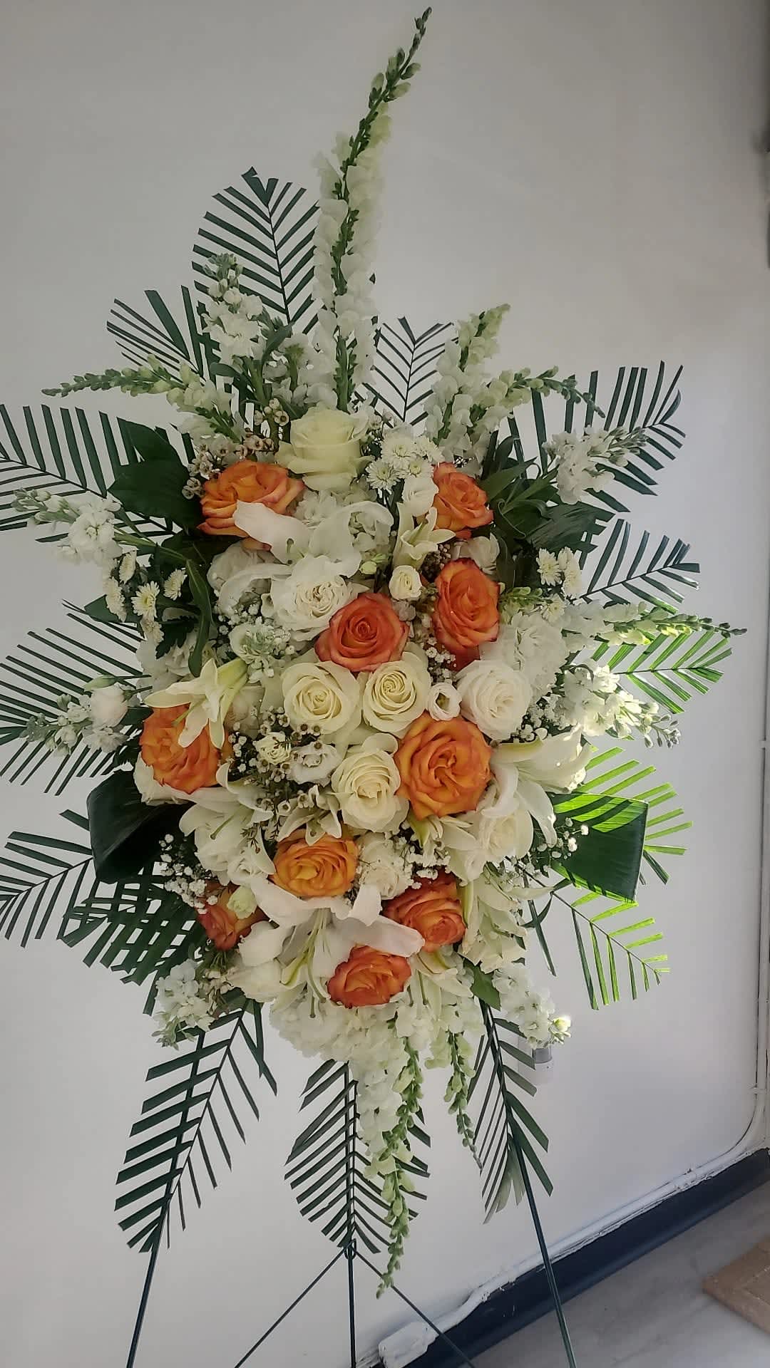 Serene Blessings (orange) by Joly's Florist - This funeral spray is pure and tranquil. Featuring a variety of orange flowers and green palms this elegant funeral spray brings a feeling of peace to it's surroundings 