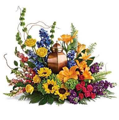 With All Our Hearts Cremation Tribute - A joyful celebration of a colorful life, this bright bouquet of hydrangea, roses and sunflowers surrounds the cremation urn with natural beauty. This colorful arrangement includes green hydrangea, yellow roses, hot pink spray roses, orange asiatic lilies, yellow sunflowers, bells of Ireland, blue delphinium, orange snapdragons, purple stock, curly willow, cedar stem, sword fern, aralia leaf, and lemon leaf. Arrangement does not include urn.