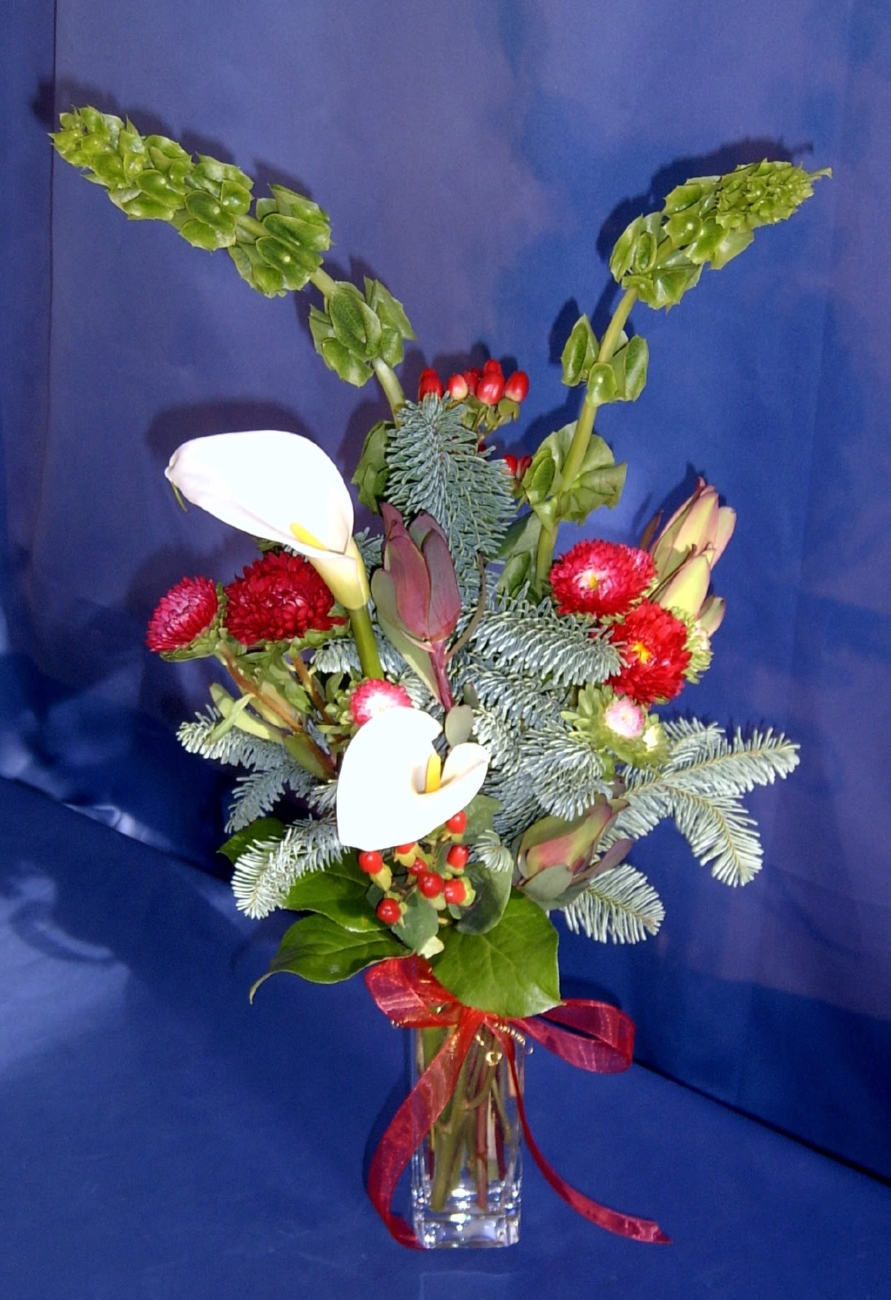 Christmas Bud Vase Christmas Bud Vase - Delightful small bud vase of cheerful Christmasy accents and items. Vase style may vary. Calla lilies only available as seasonally able and provided when minimum 3 days' notice is given. Other premium flower will be substituted if needed, such as a rose, tulip or freesia.