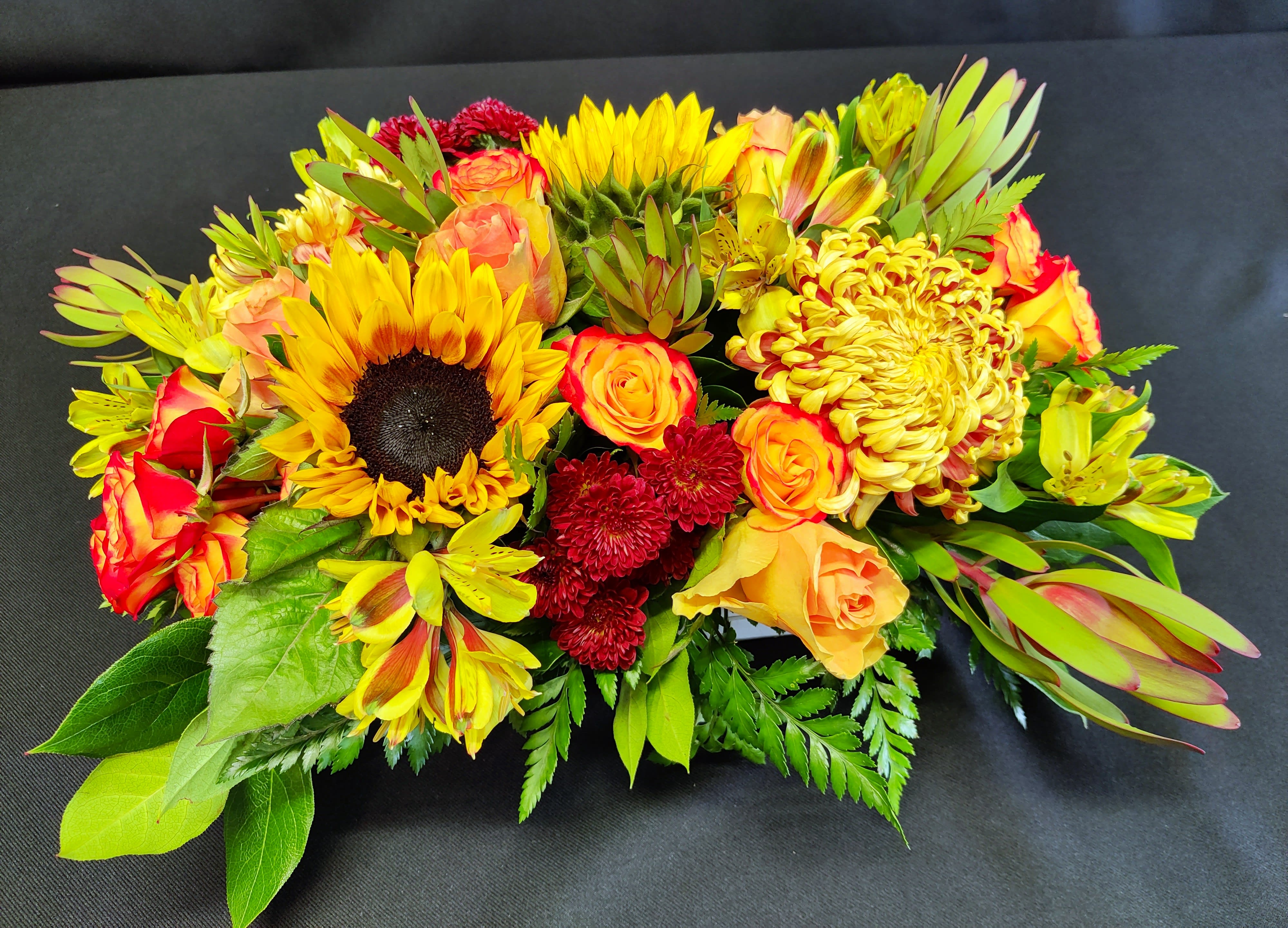 Robust fall sunflower centerpiece - A thickly arranged centerpiece of fall flowers in a low design dish. Colors and items will vary. Designer's choice of flowers. Order well in advance of Thanksgiving for best fall colors.