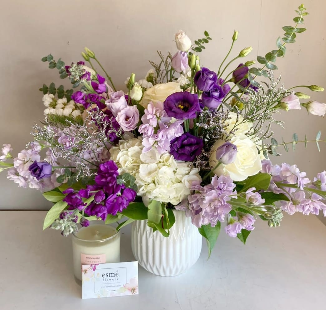Clemence Clemence - This enchanting composition artfully combines white blossoms with the regal allure of deep purple flowers. White radiates purity and grace, while velvety purple and delicate lavender add a touch of sophistication. The arrangement is beautifully accented with silver eucalyptus leaves in a premium white ceramic vase.