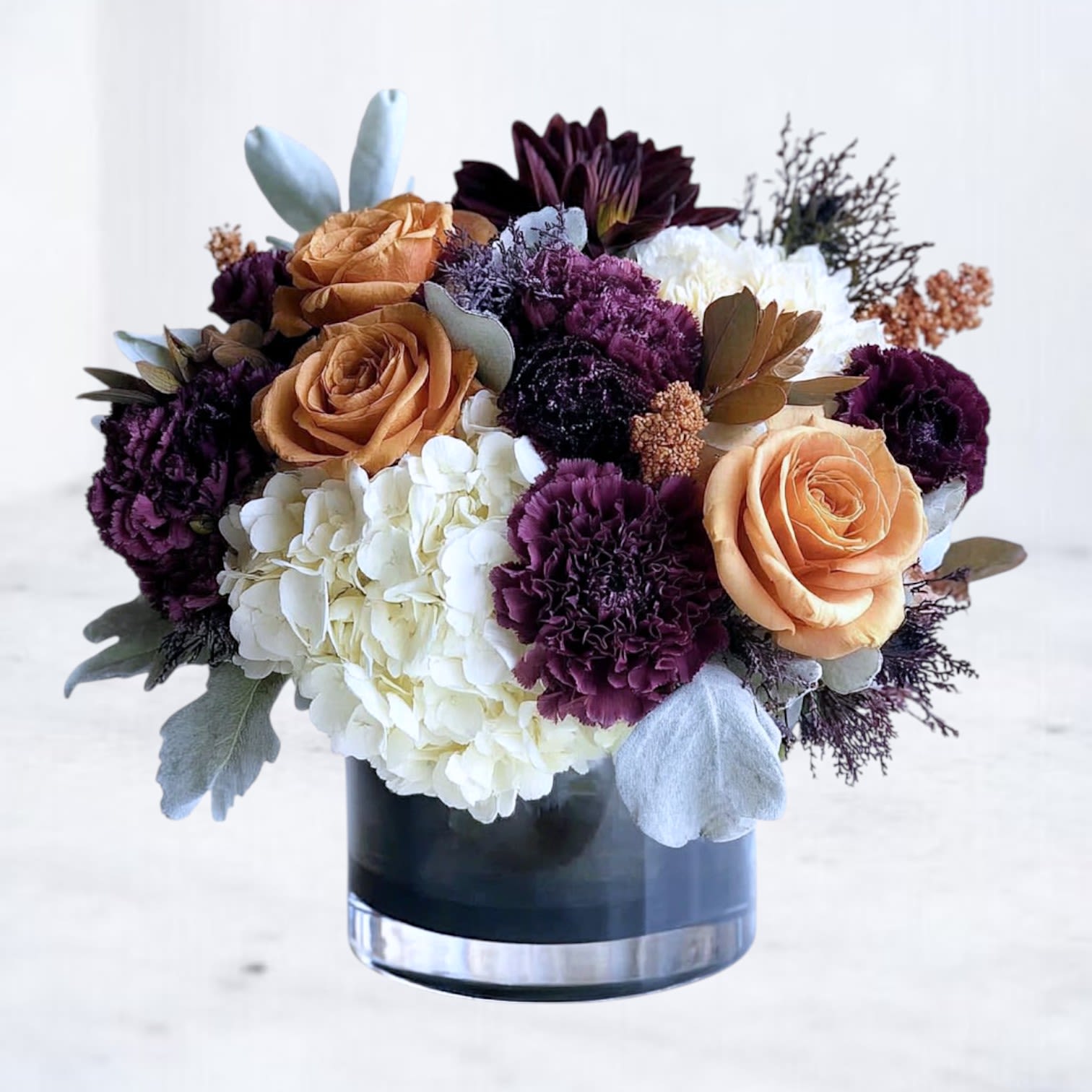 Fallowlight Fallowlight - Where stillness meets warmth — Fallowlight embodies the quiet beauty of change. This artful arrangement features rich purple carnations, peachy-toned roses, and ivory hydrangea arranged in a modern vase. Each flower is placed with intention, creating a balance between depth and softness, shadow and glow. Inspired by autumn’s muted light and the hush before renewal, this design speaks of reflection, love, and resilience. Whether sent as a thoughtful gesture, a comforting expression, or a statement of refined taste, Fallowlight feels timeless — graceful in any season, unforgettable in any space.